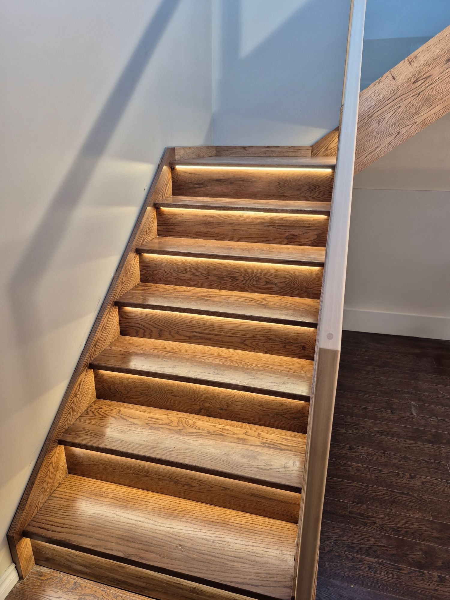 Elegant oak staircase with LED under-tread lighting installed, creating a warm glow on dark hardwood floors.