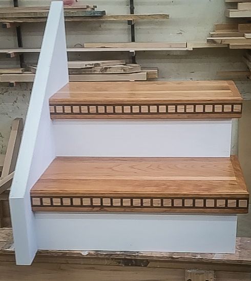 Custom oak stair treads with decorative carved square pattern border detail against white risers in a workshop.
