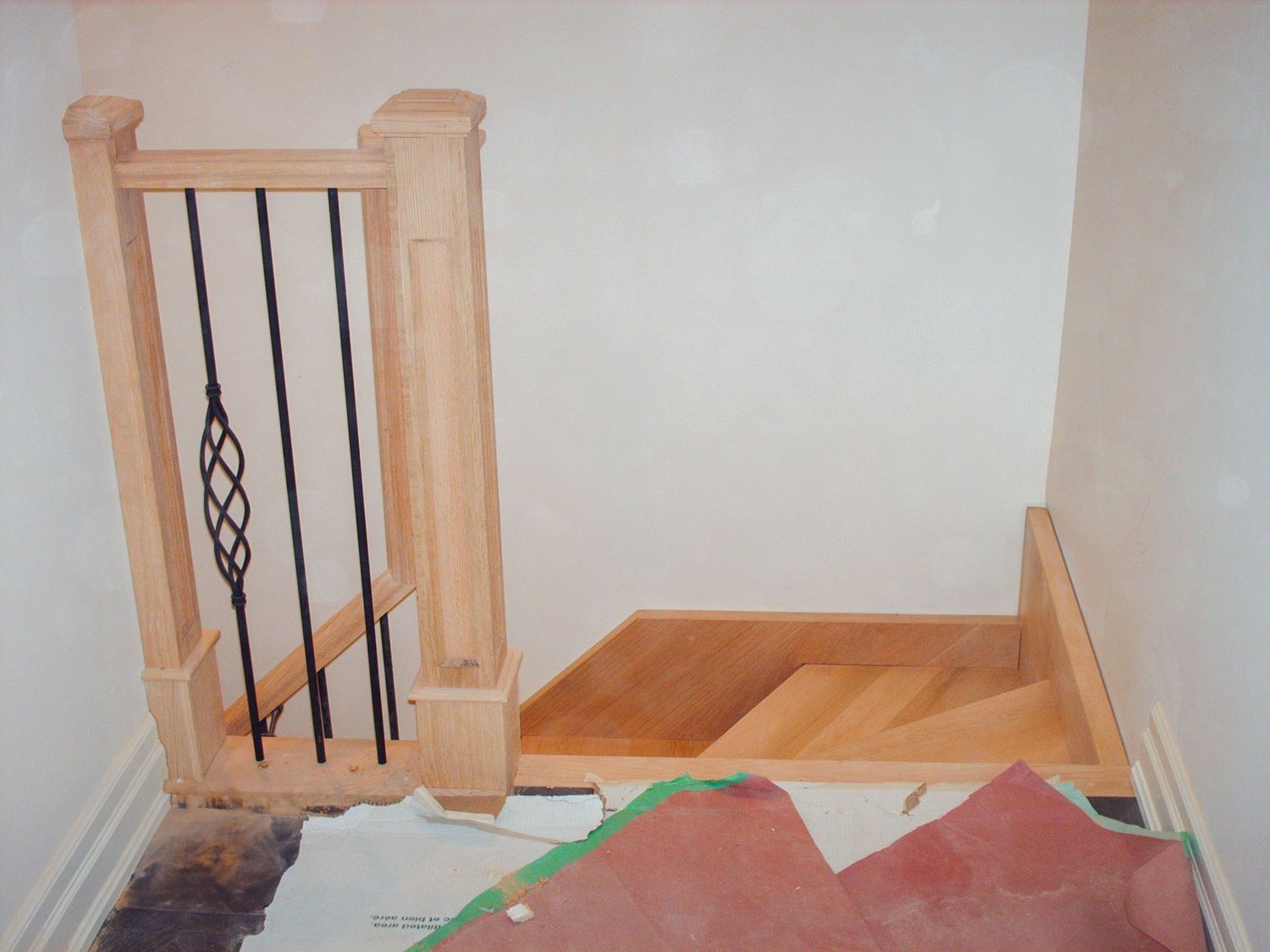 Wooden staircase landing with decorative  black metal pickets and  a wooden newel post during home construction.