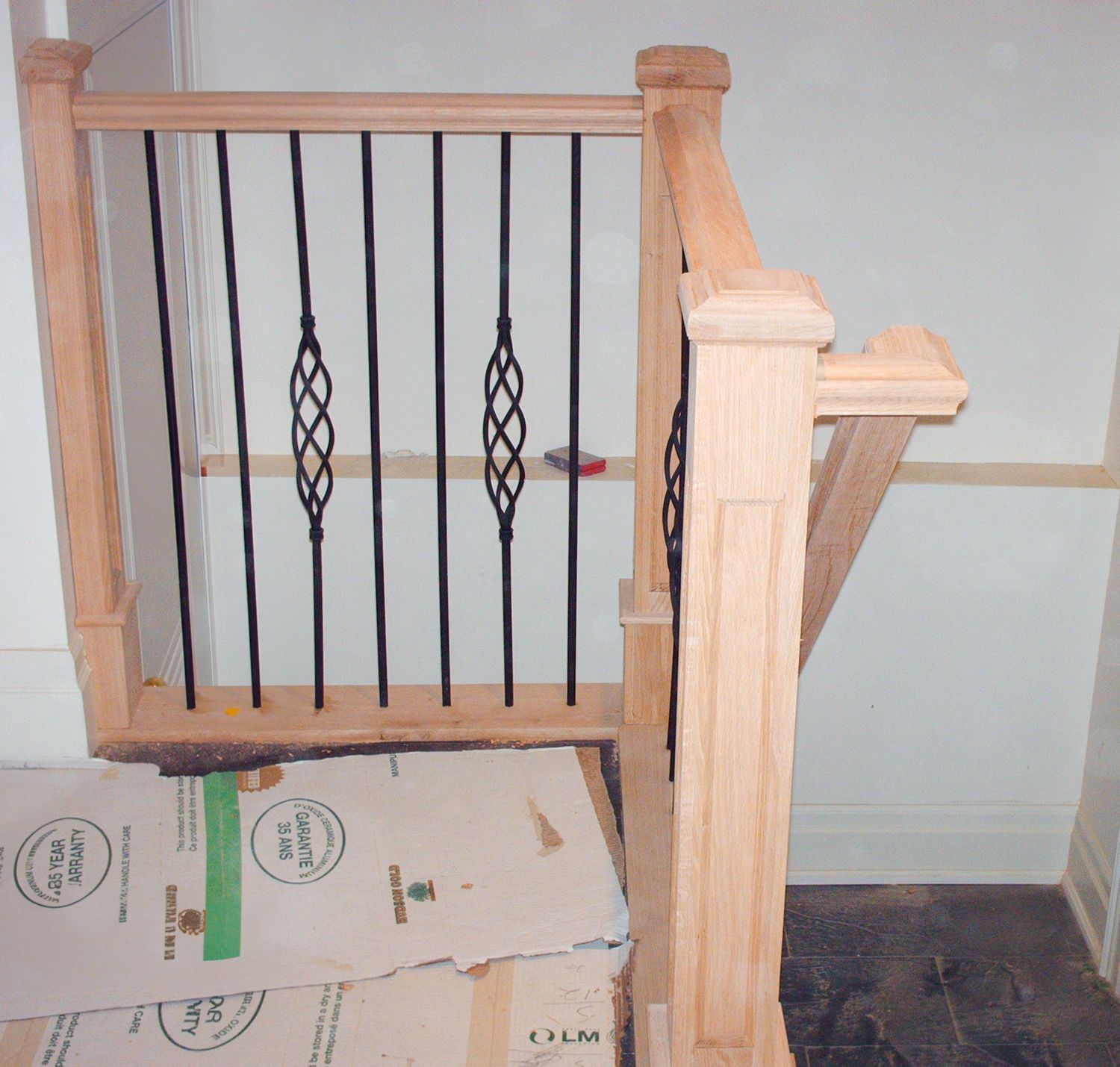 Close-up of light wood newel post with decorative twisted metal spindles during stair installation.