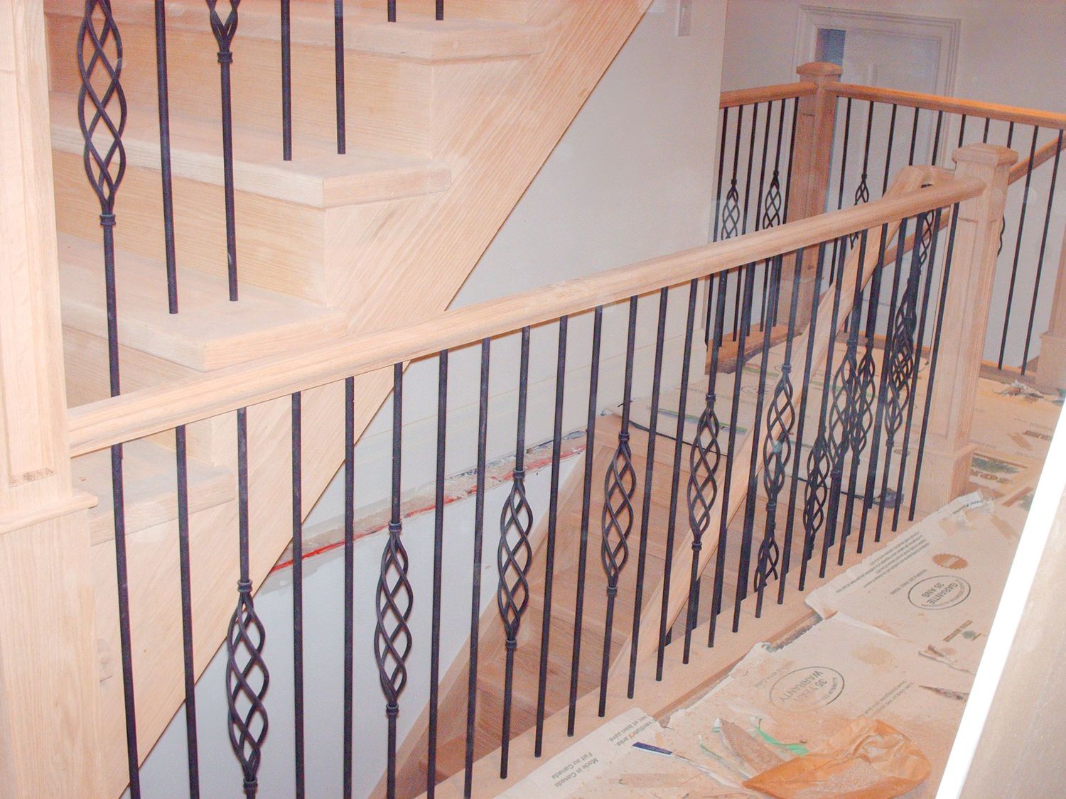 Light wood stair railing with decorative black metal spindles installed along upper landing hallway.