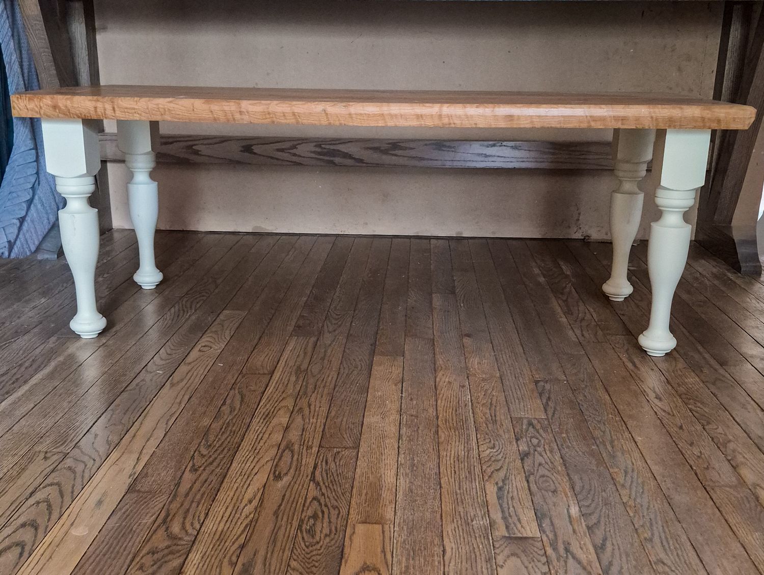 Rustic White oak farmhouse coffee table with natural wood top and distressed white turned legs on hardwood floor.