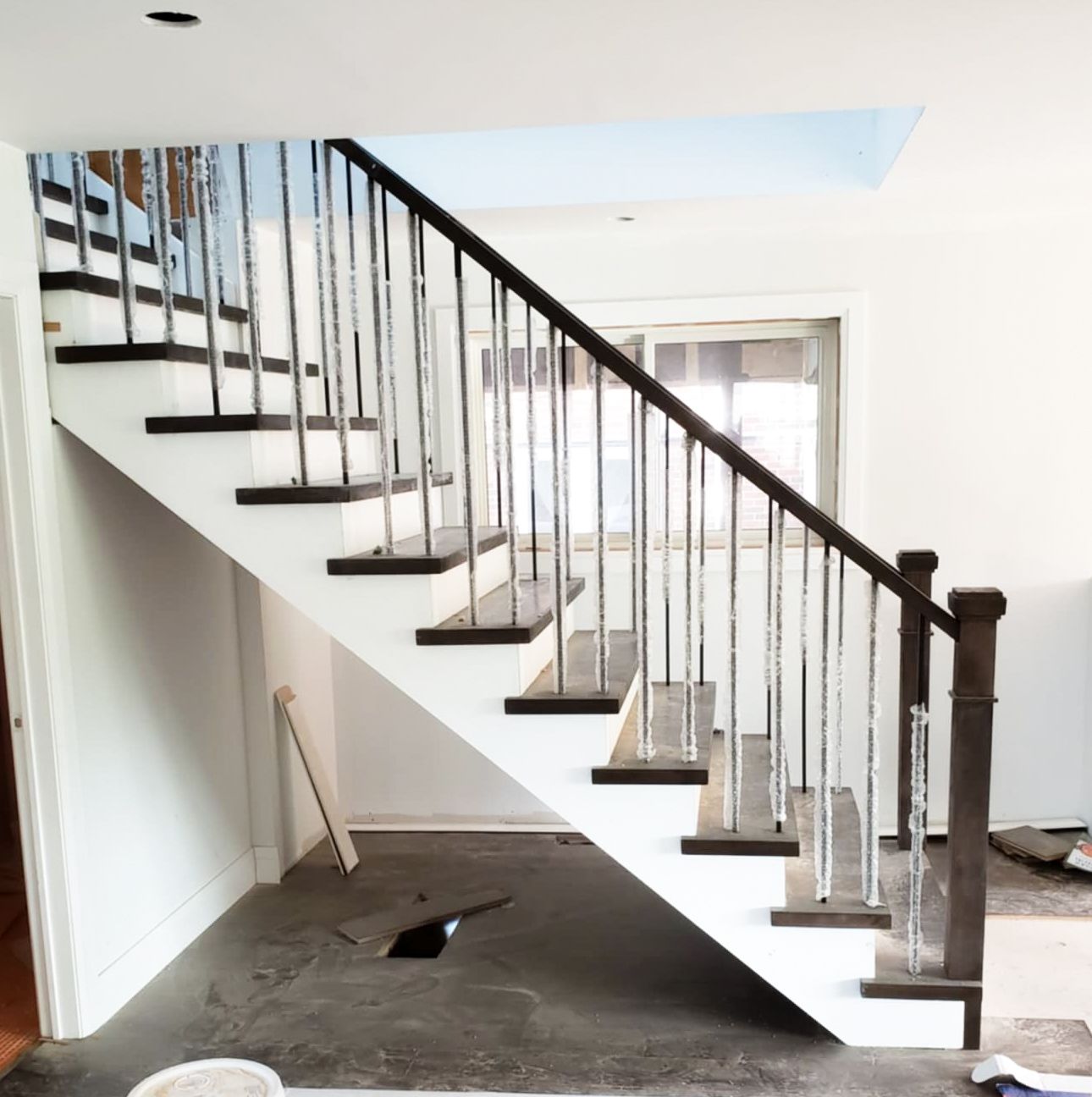 Straight staircase with dark wood treads, metal balusters, and dark handrail in a modern home renovation.