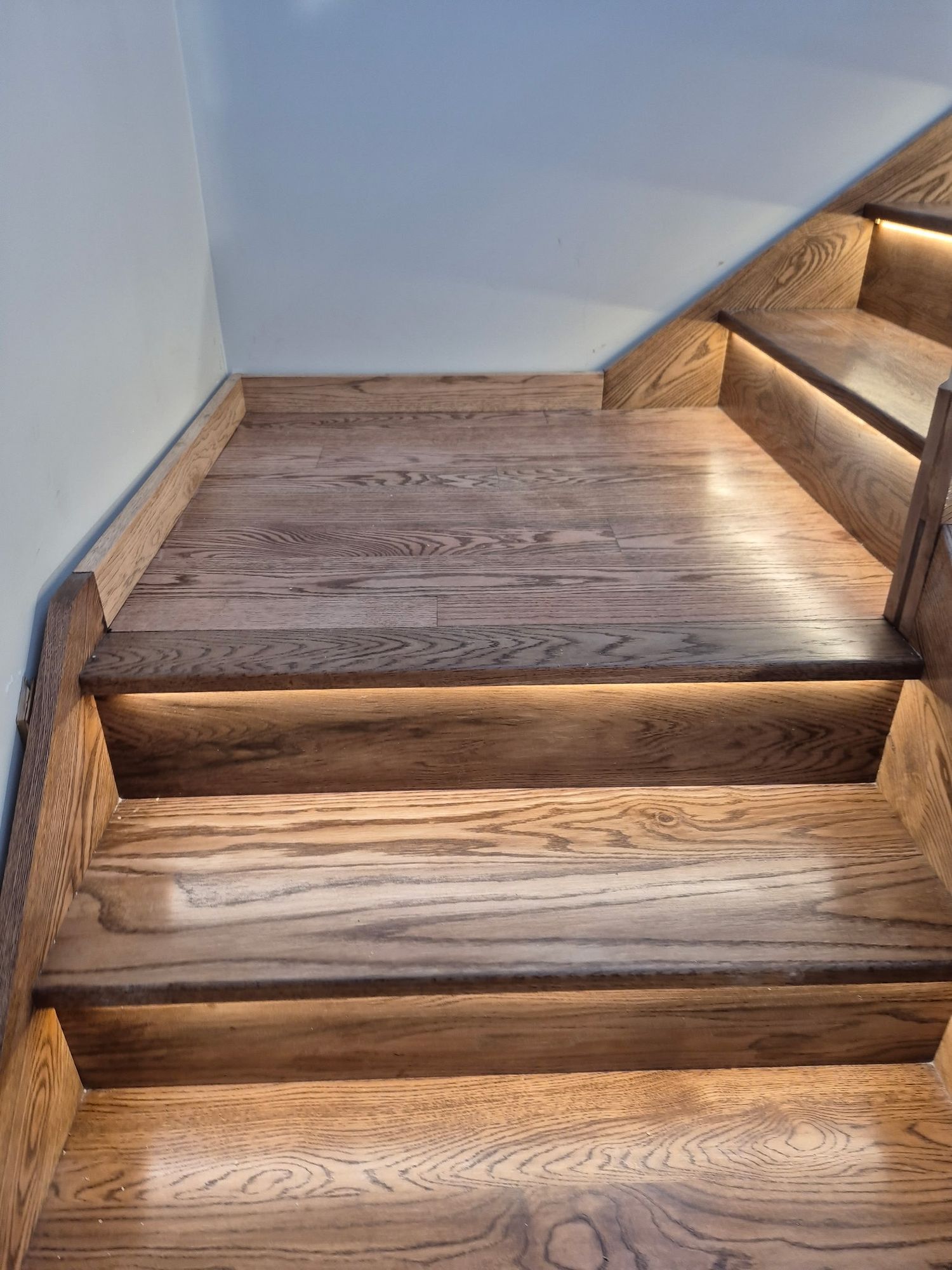 Finished oak hardwood staircase with warm brown stain and subtle LED lighting under each tread.
