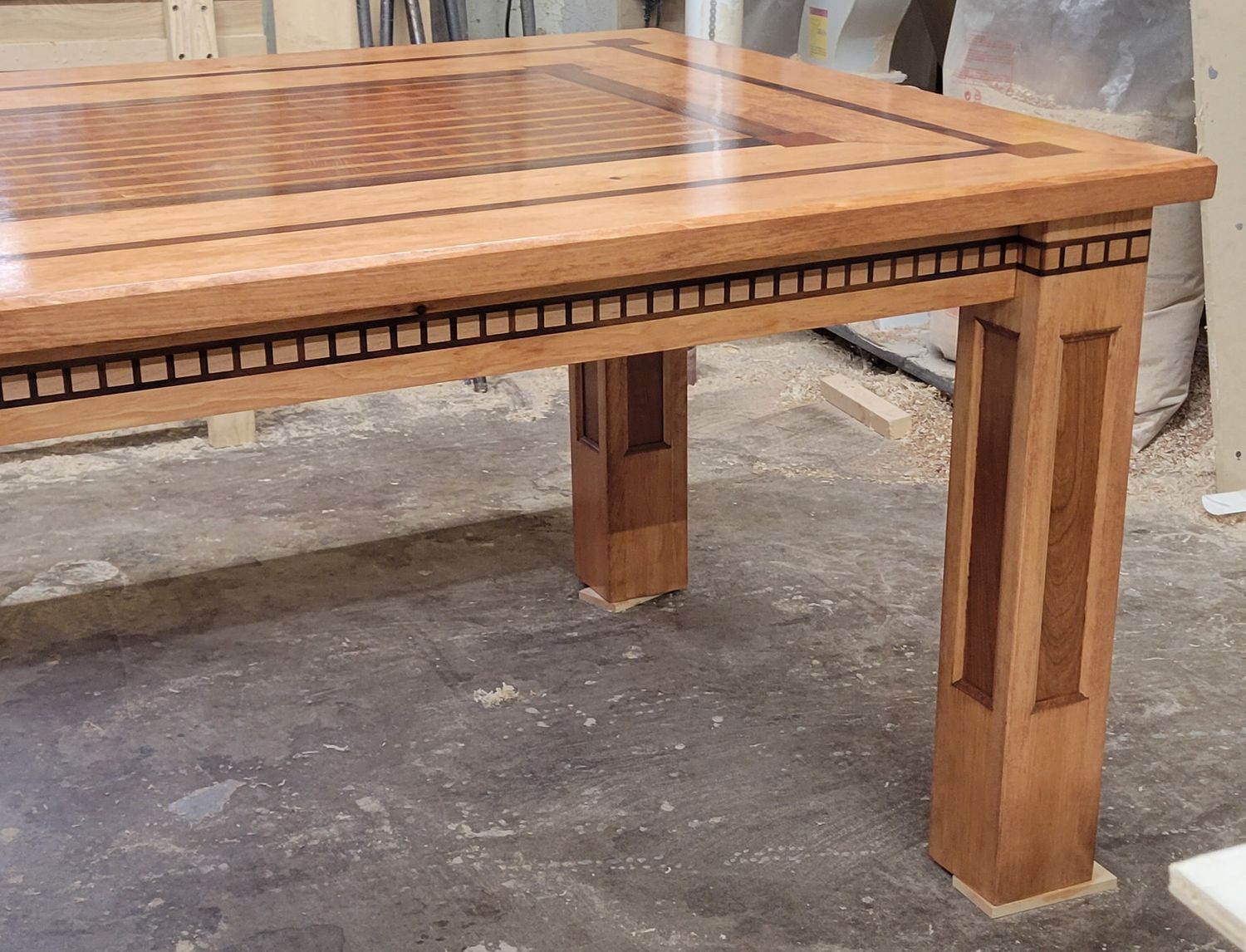 Custom handcrafted wooden dining table with decorative inlay border and solid square legs.