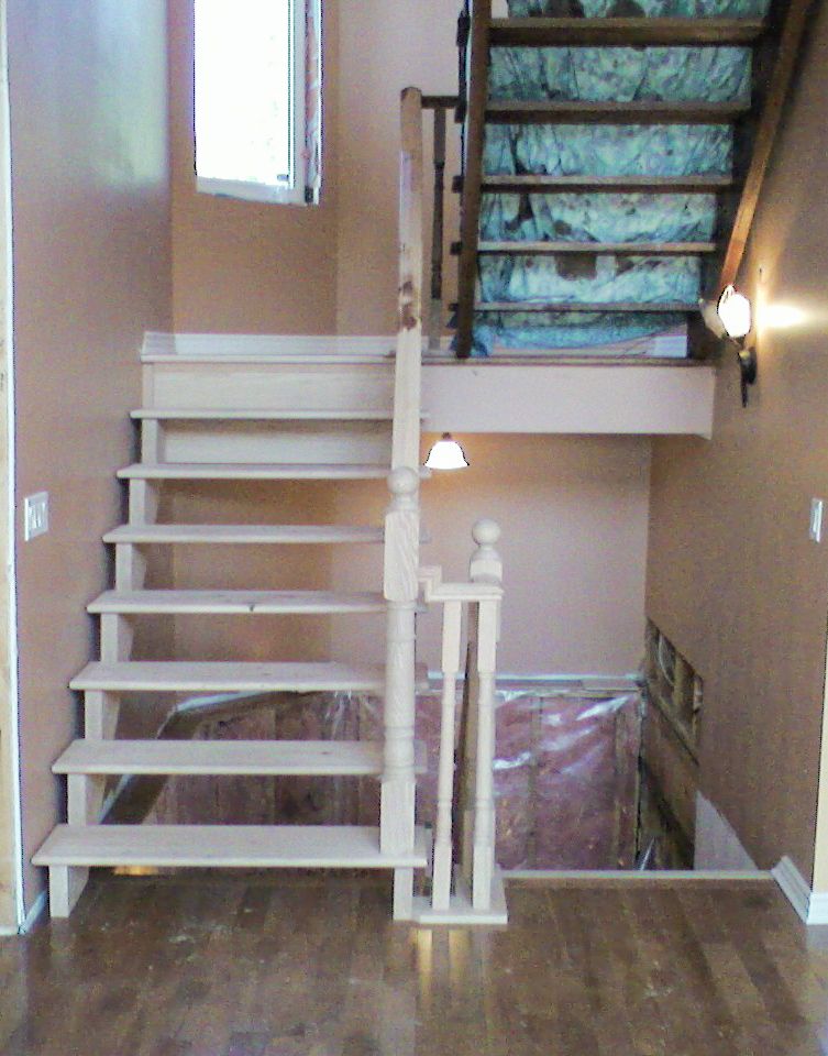 Newly installed open-riser wooden staircase with white newel post in a home under renovation with hardwood floors.