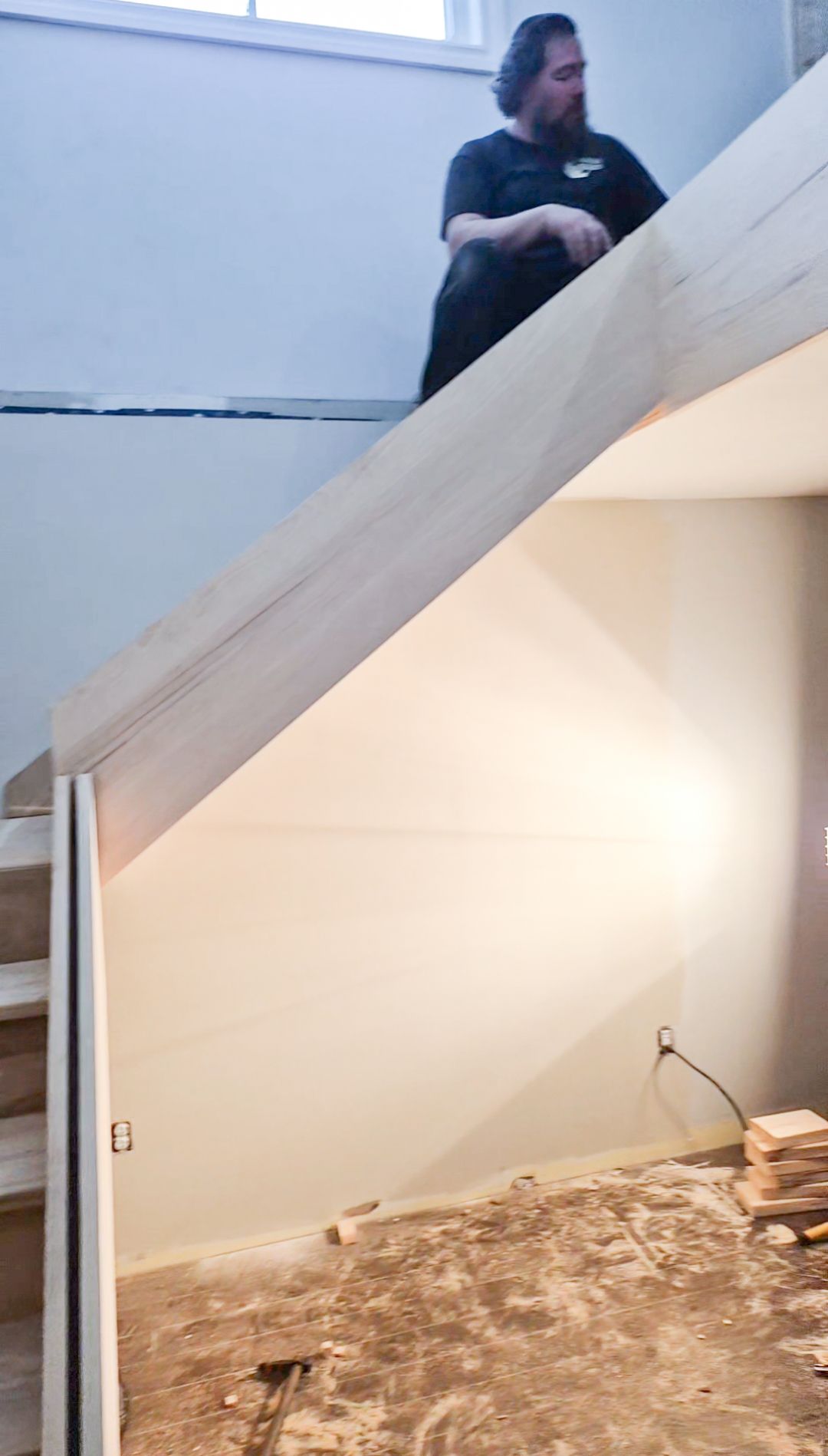 Carpenter installing wooden handrail on open-concept staircase with white painted stringers during home renovation.