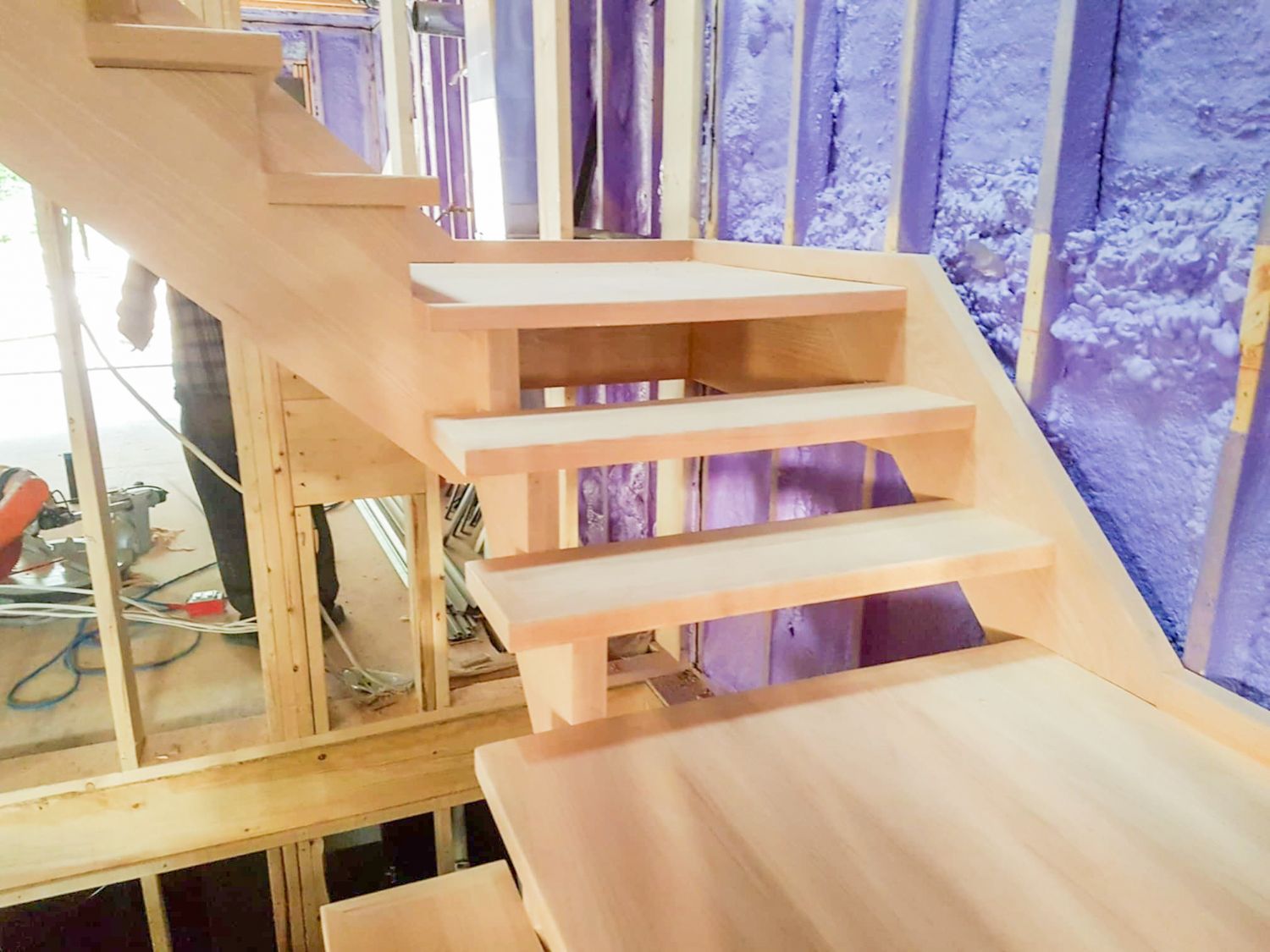 Unfinished wooden open-riser u- shaped staircase under construction with red oak treads in a framed interior.