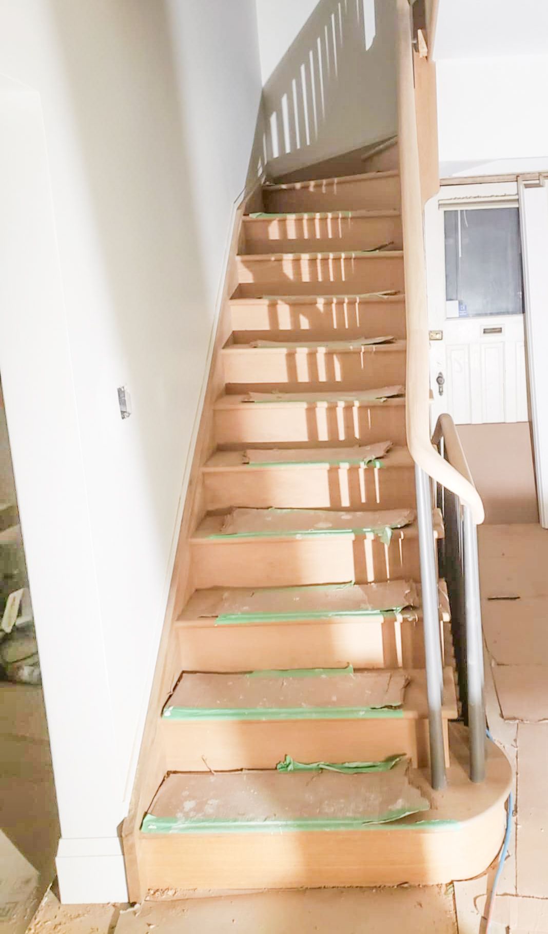 Straight wooden staircase with protective green tape on treads during home renovation and construction.