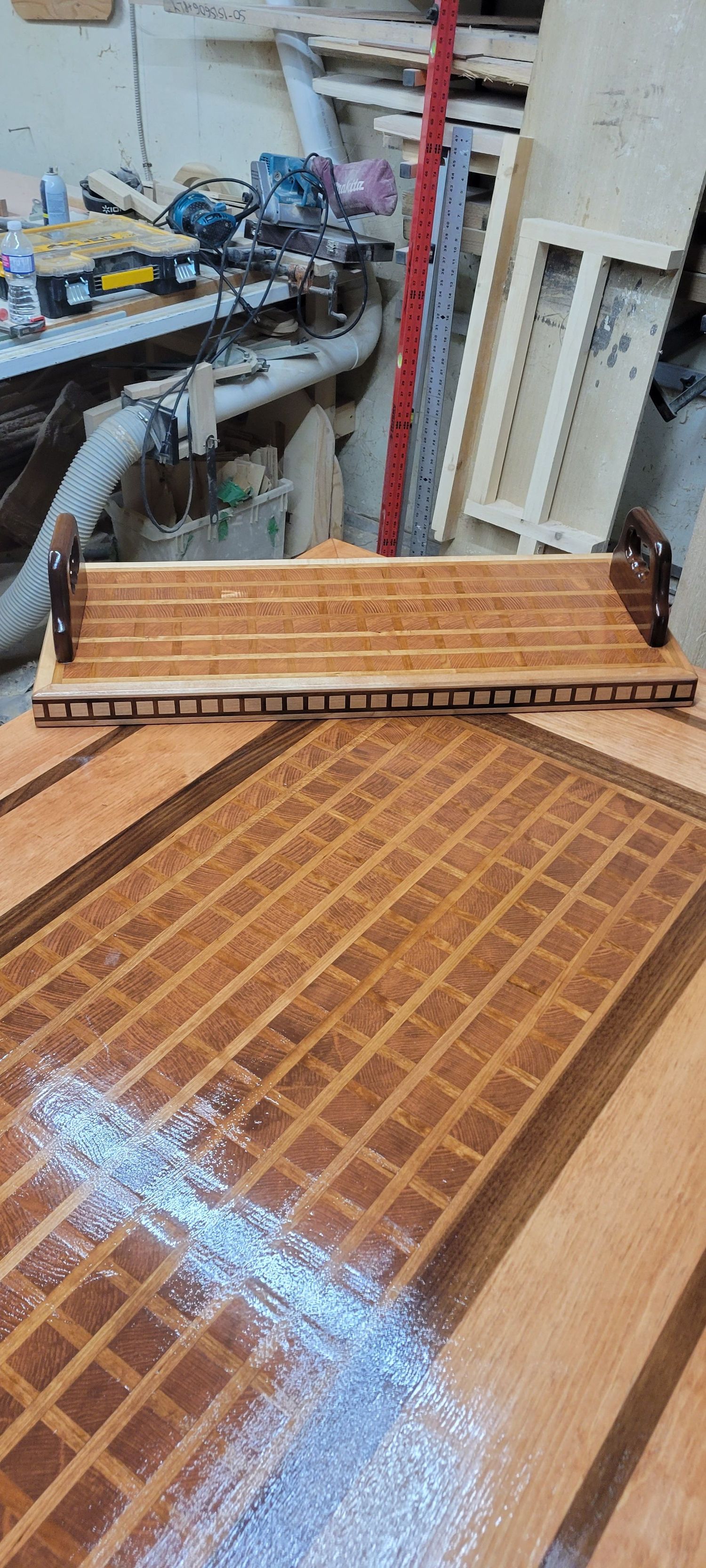 Handcrafted wooden serving tray with grid inlay patterndisplayed in woodworking workshop.