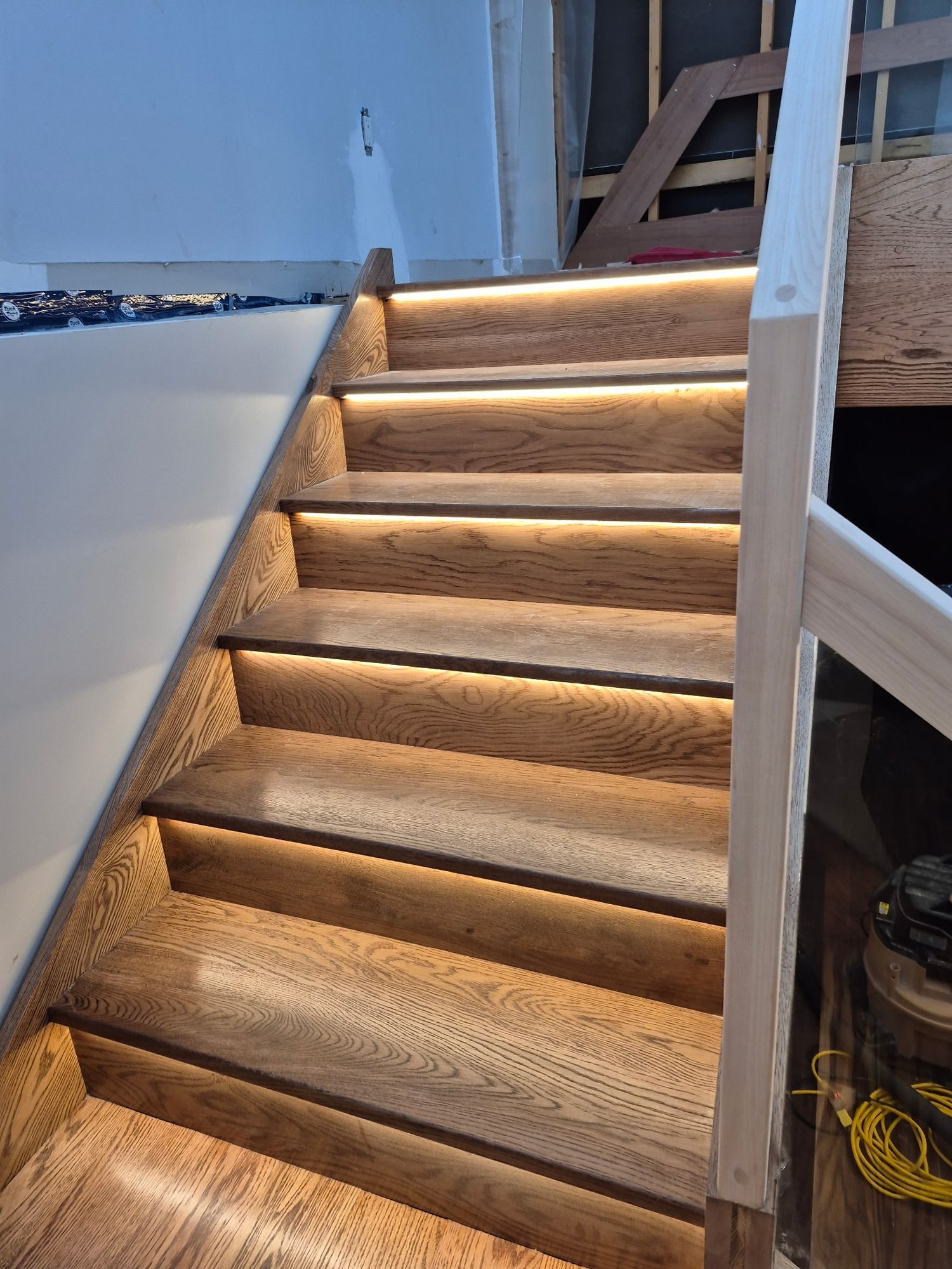 Modern staircase with oak treads and LED strip lighting under each step during home renovation.