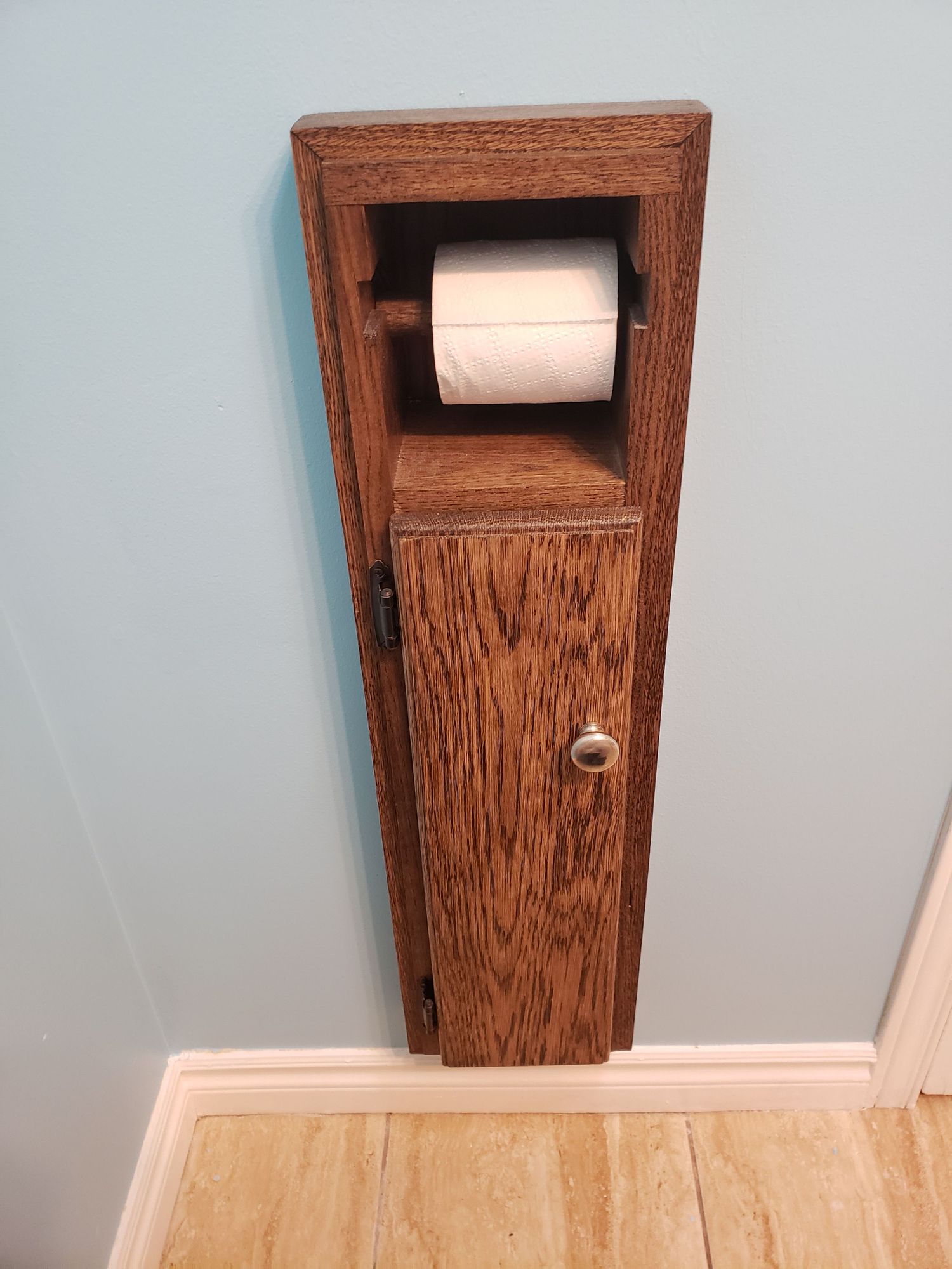 Custom oak build-in toilet paper holder cabinet with door and storage compartment in bathroom.