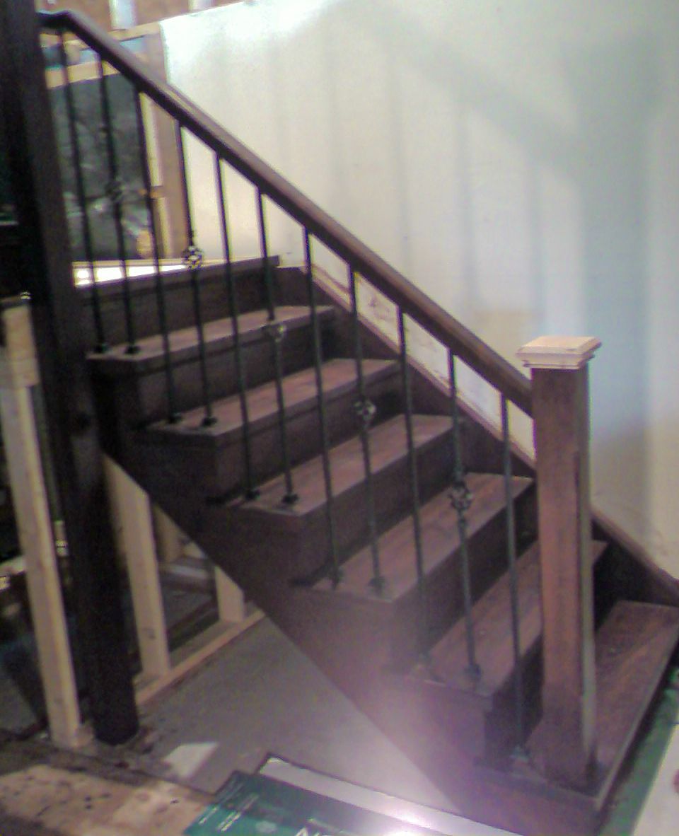 Dark stained wooden staircase with black metal spindles and wood handrail in a home interior setting.