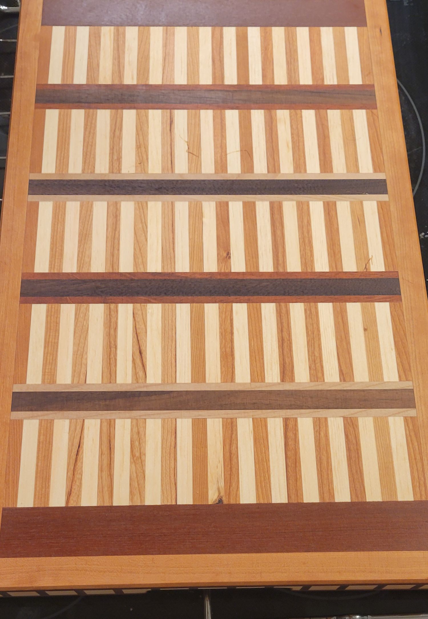 Handcrafted wood cutting board with alternating light and dark wood stripes in a striped pattern design.