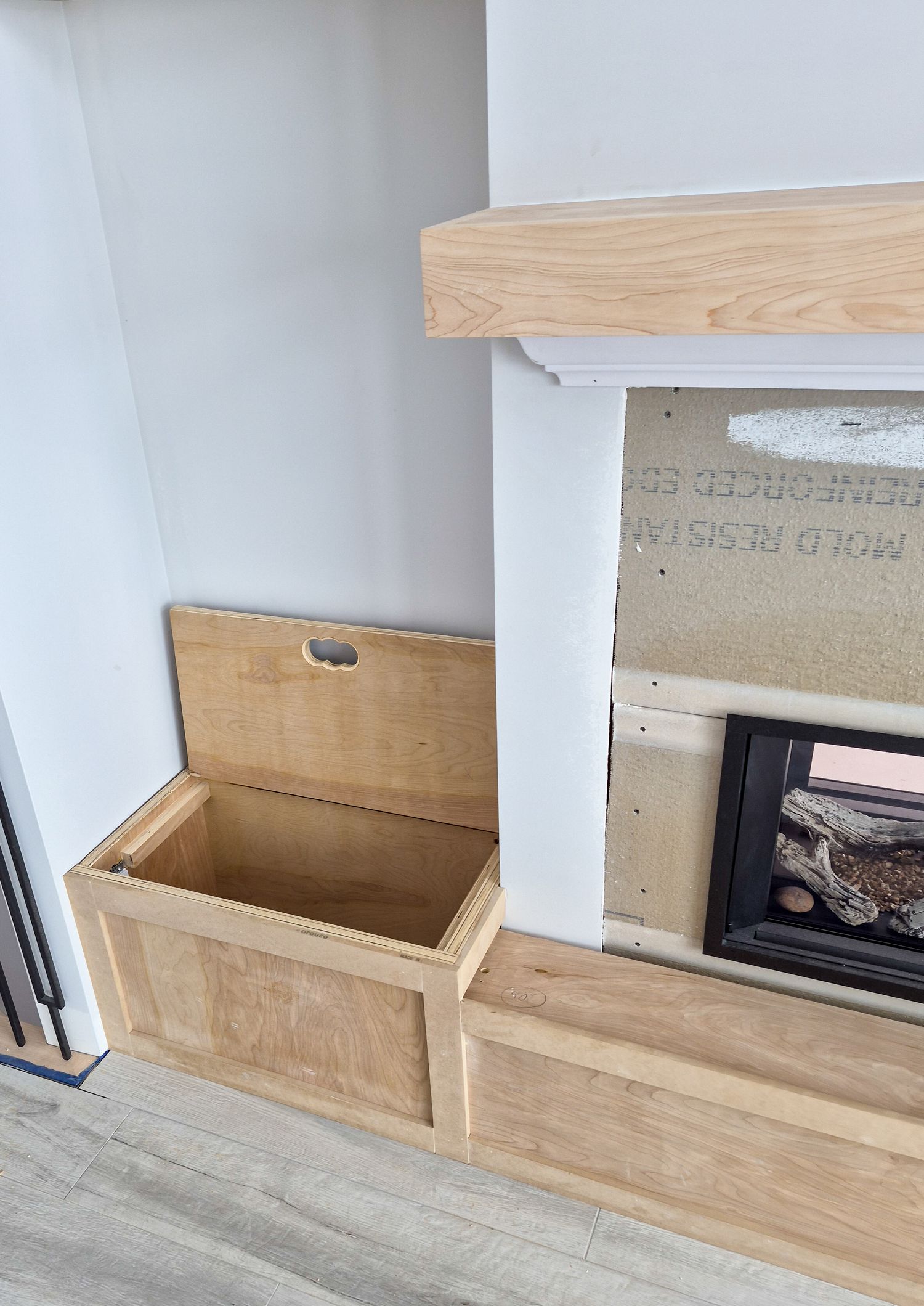 Custom built-in wooden storage bench with lift-top lid beside a fireplace during home renovation.