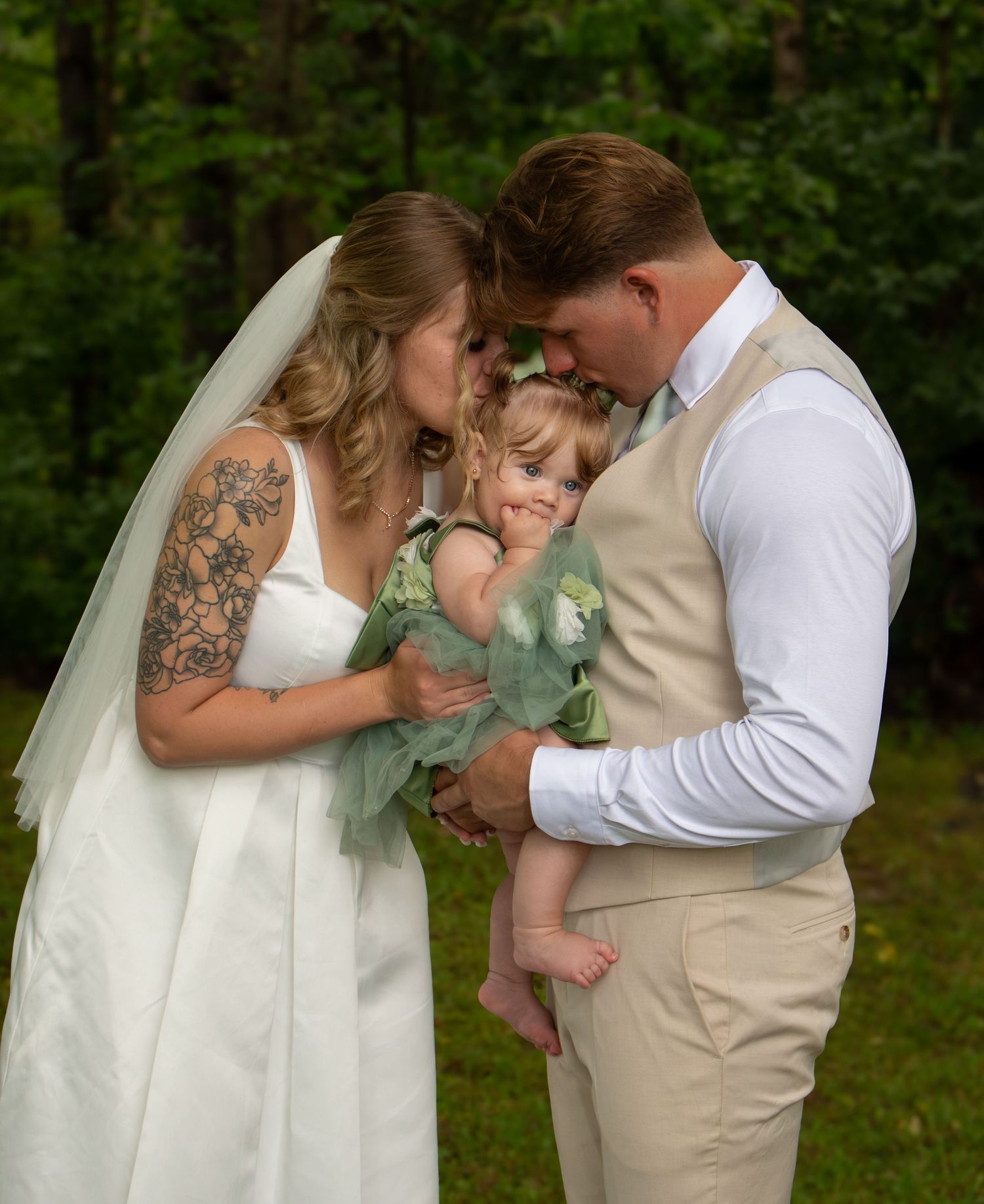 Bride and groom holding their young daughter during their beautiful outdoor wedding.