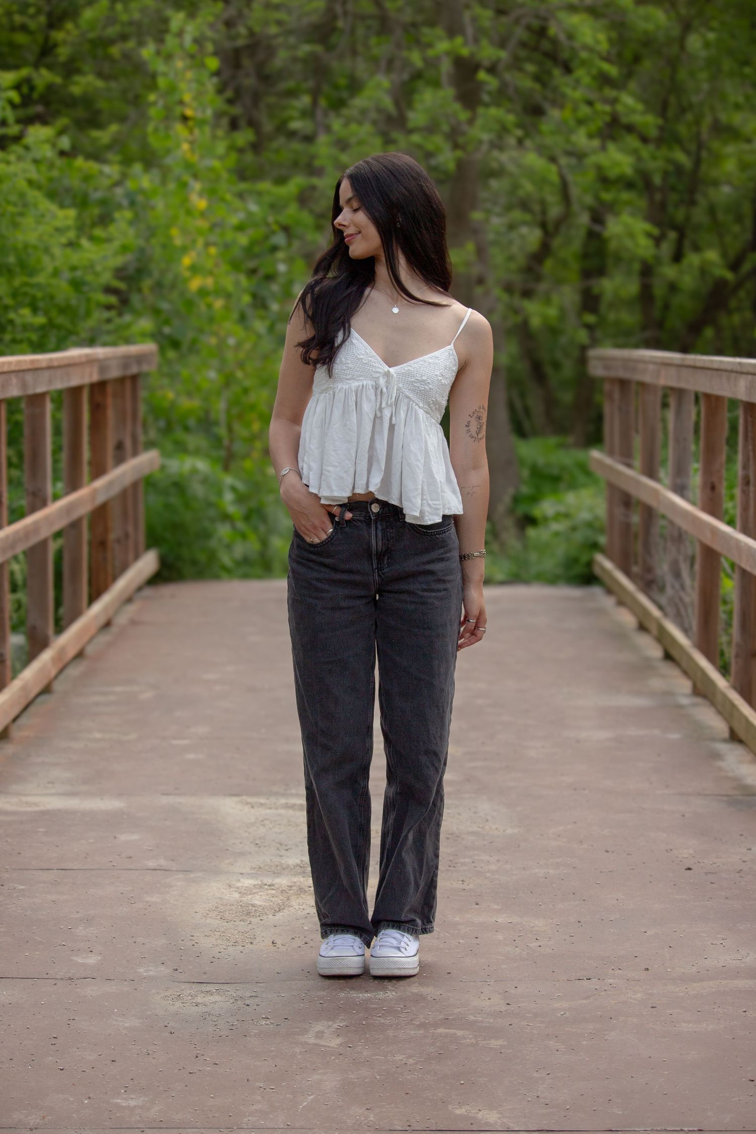 Young woman portrait session looking away on a bridge surrounded by beautiful greenery.