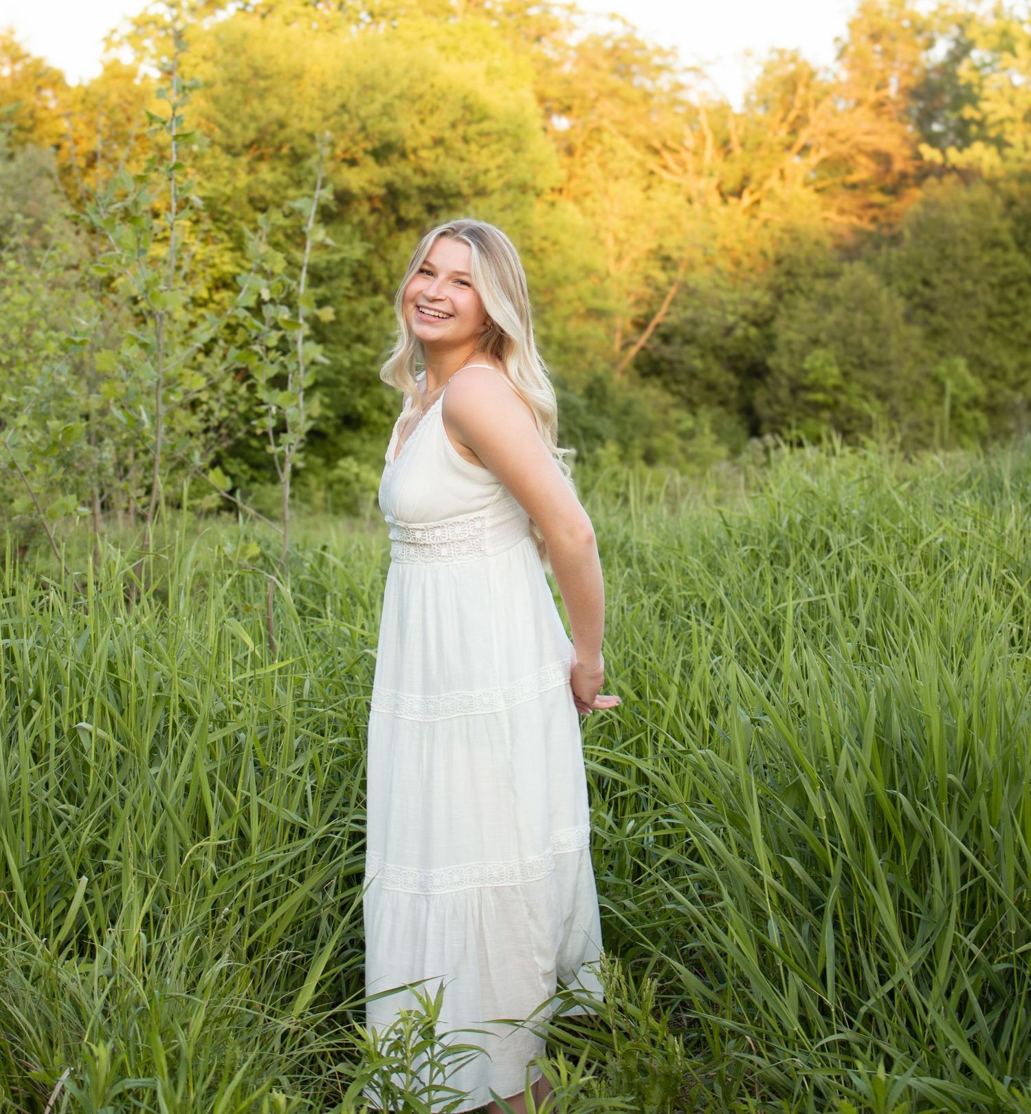 Beautiful young high school graduate posing in a field during golden hour.