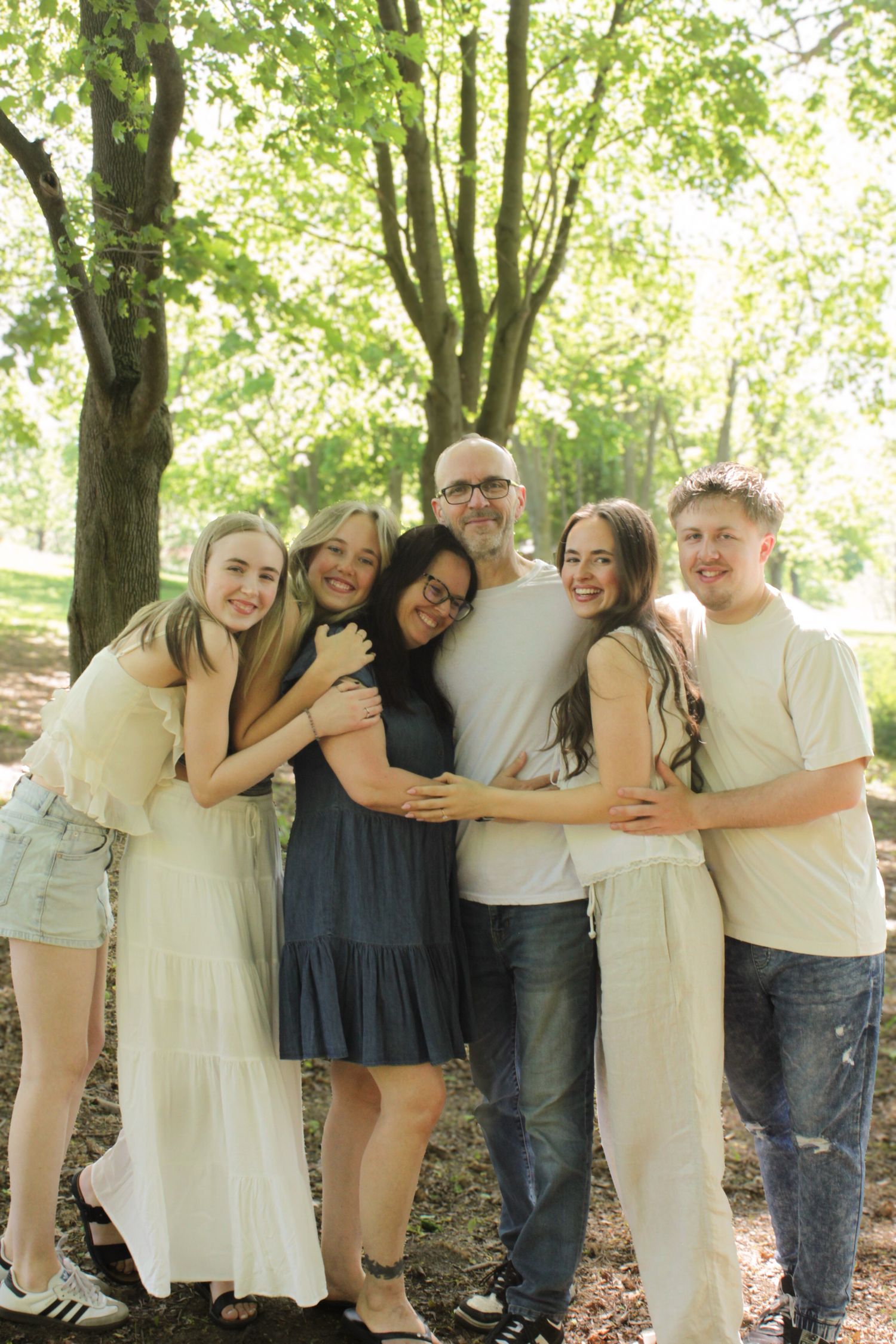 Family standing beneath the trees all snuggled in tightly.