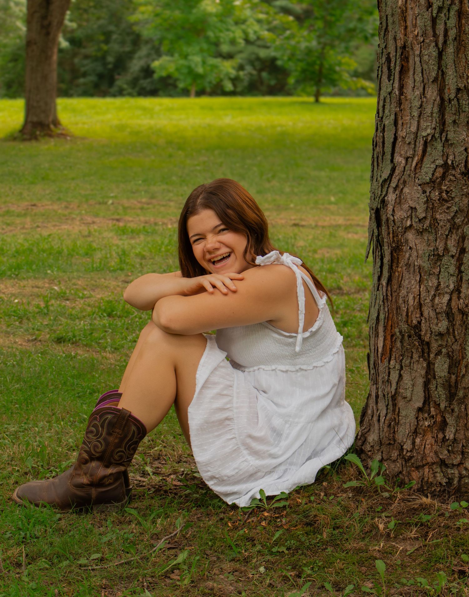 Beautiful young girl sitting laughing beneath a tree during an outdoor friend session where we added in some portraits.