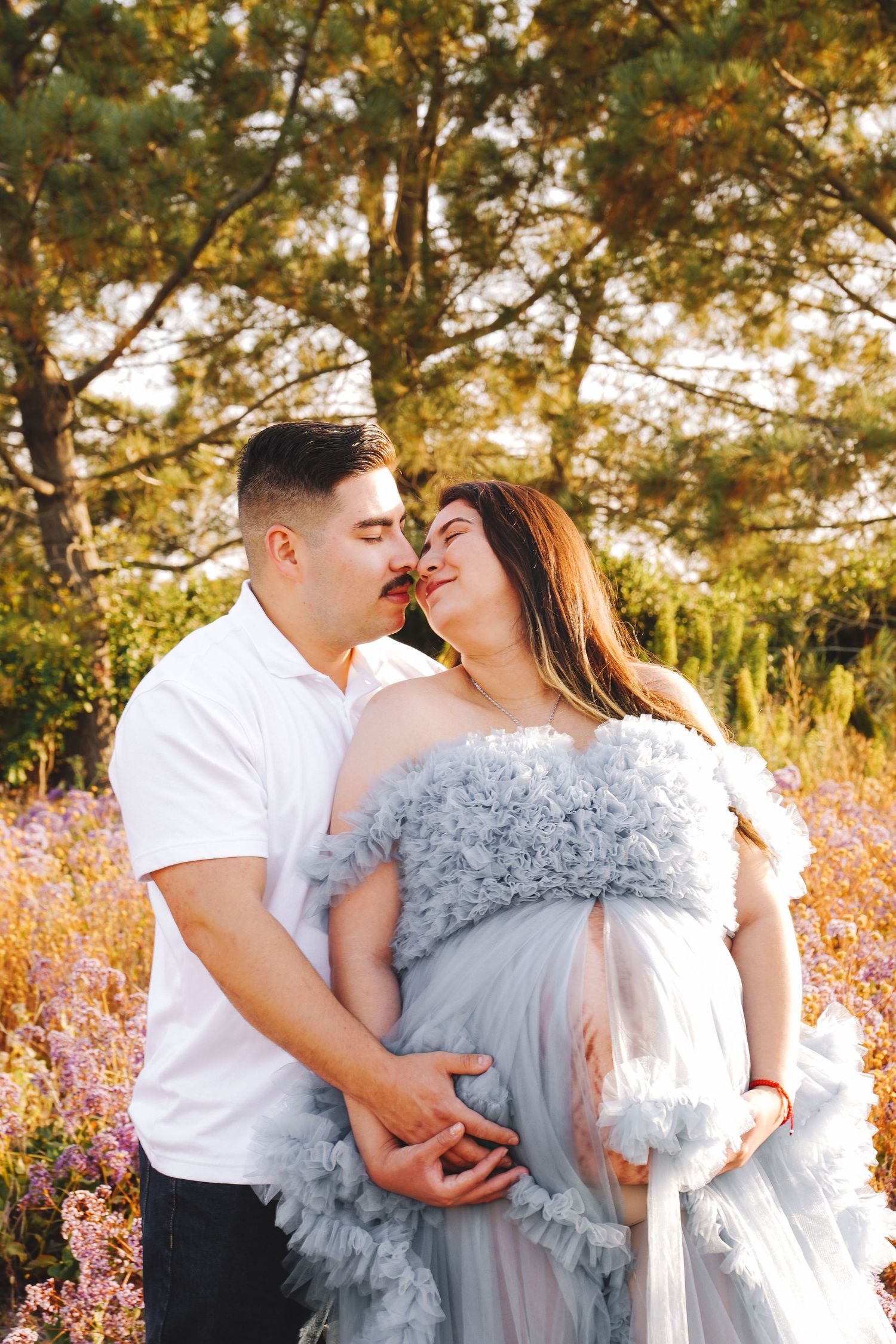 Romantic couple embraces in a dreamy outdoor setting with golden sunlight filtering through autumn trees and wildflowers.