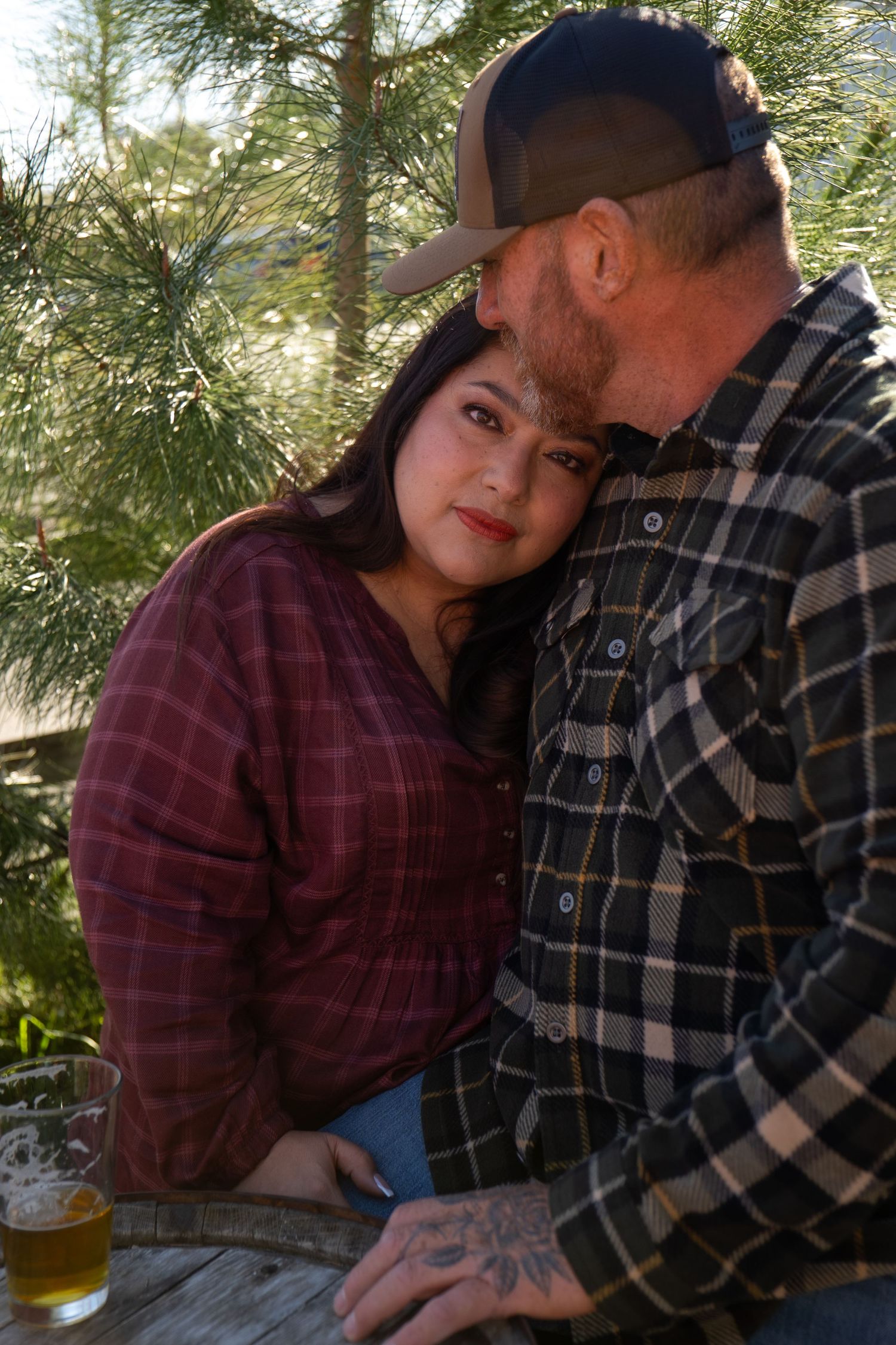 Two people in plaid shirts leaning close together at a rustic outdoor setting.