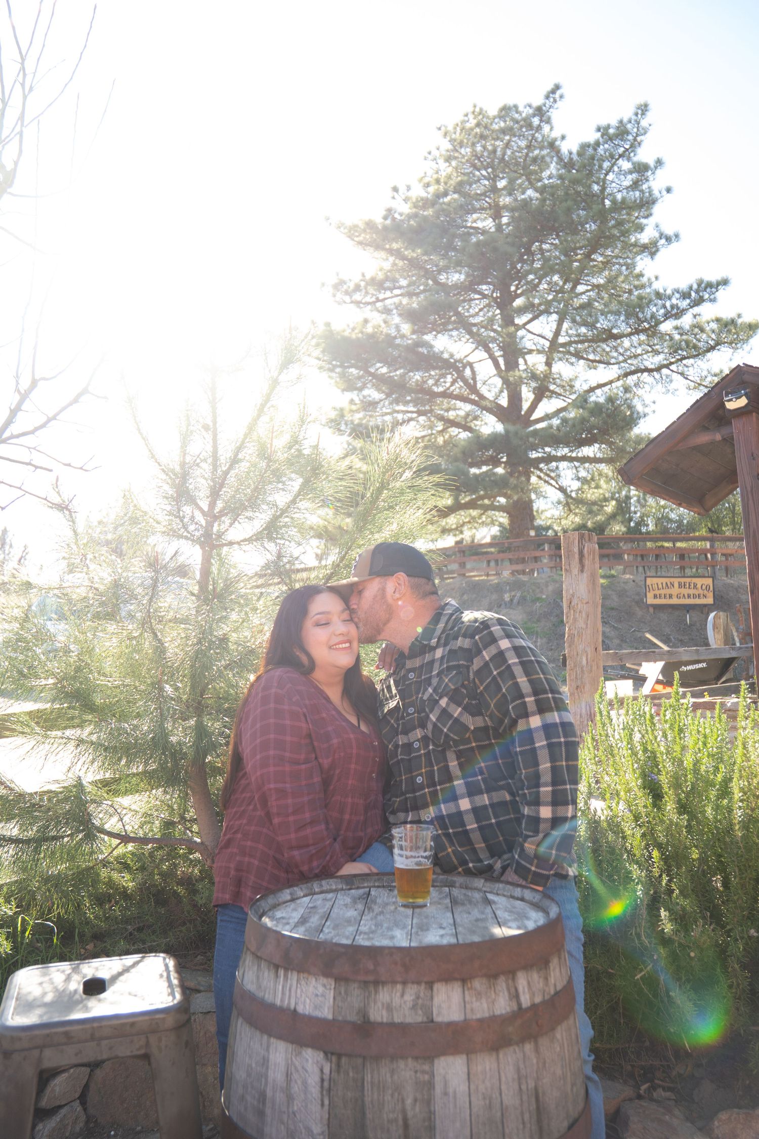 Couple sharing a romantic moment at an outdoor bar with wooden barrel tables at sunset.
