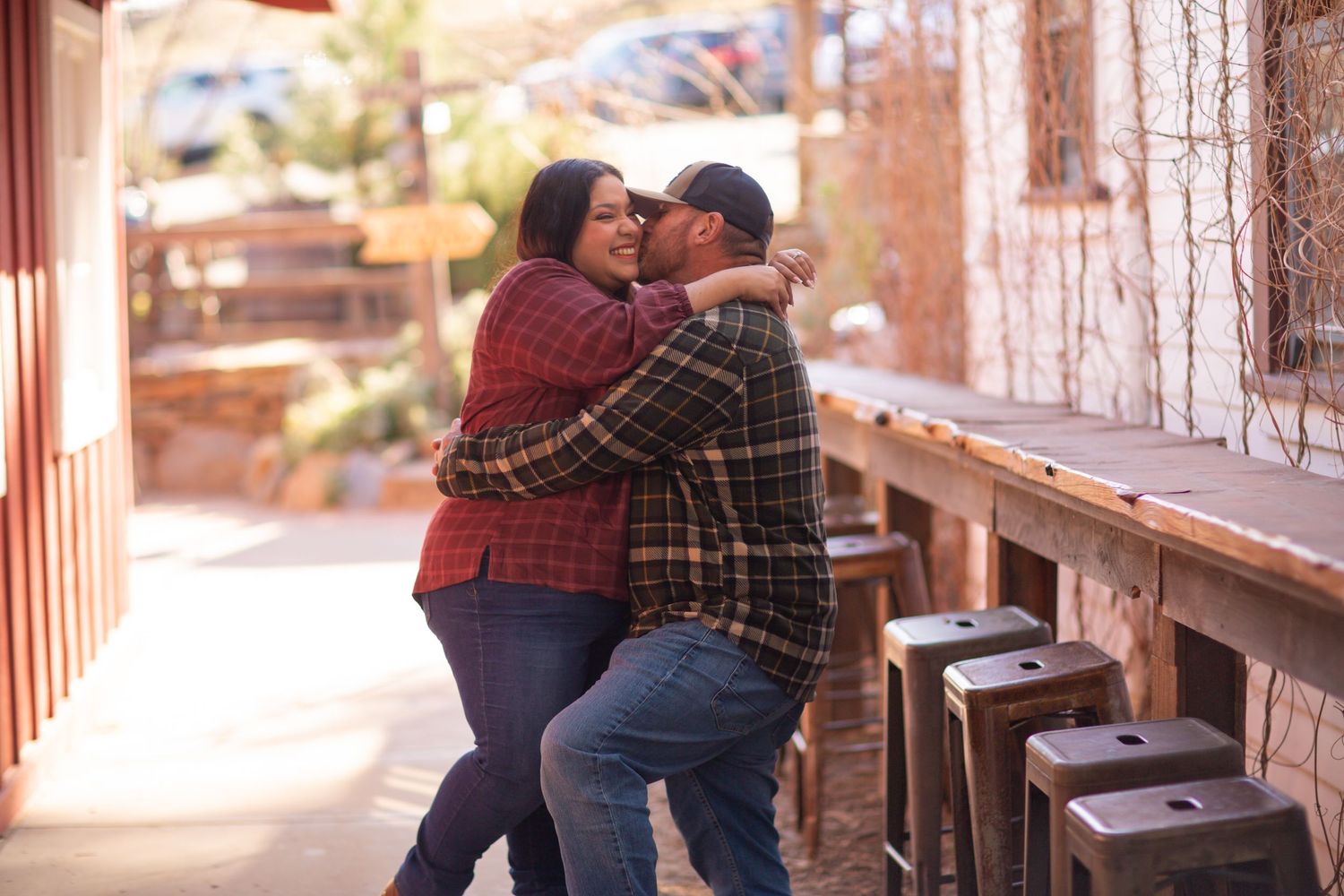 Couple in plaid shirts embracing on rustic wooden porch during outdoor photoshoot.