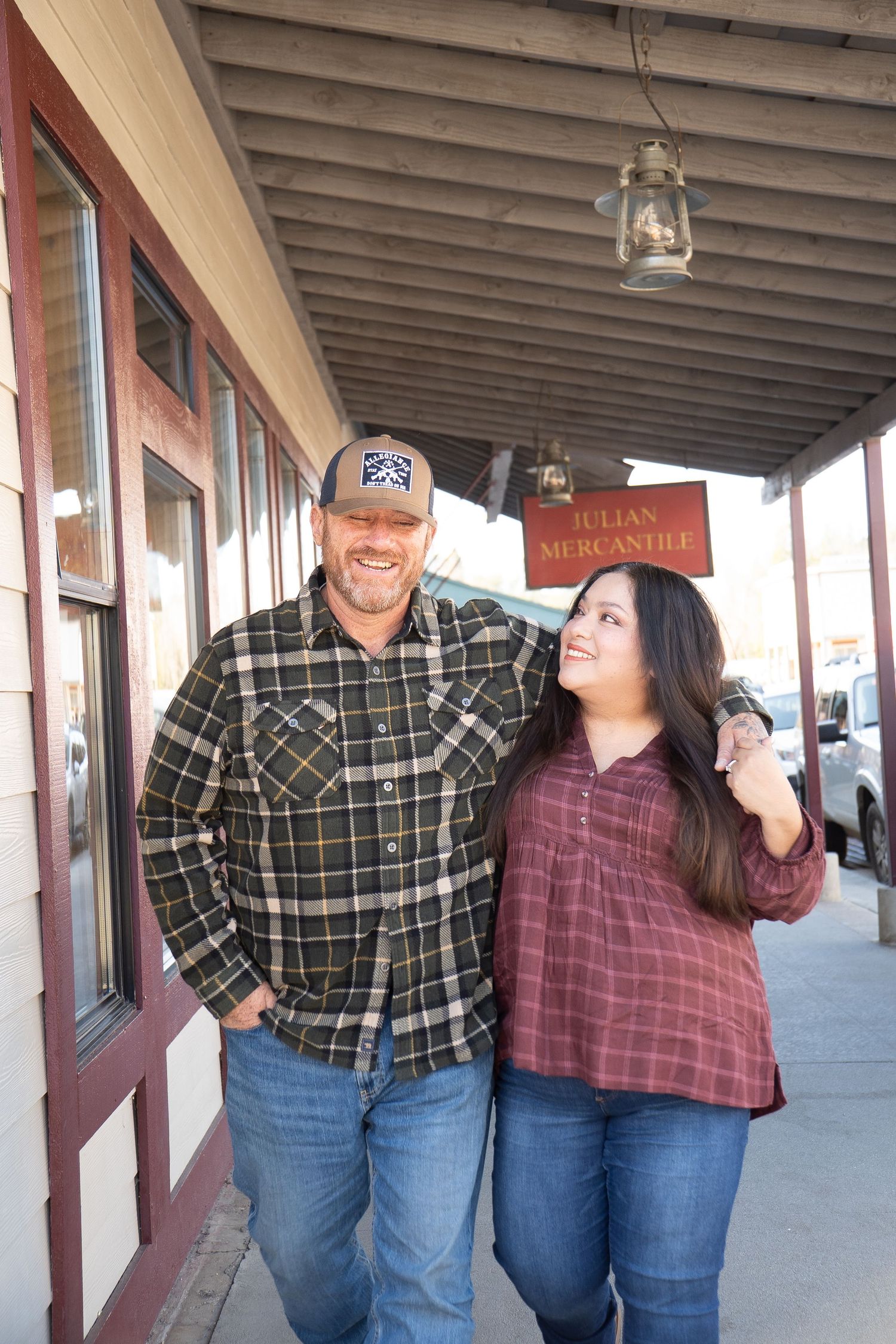 A couple in matching plaid shirts and jeans share candid moments while posing along a covered walkway.