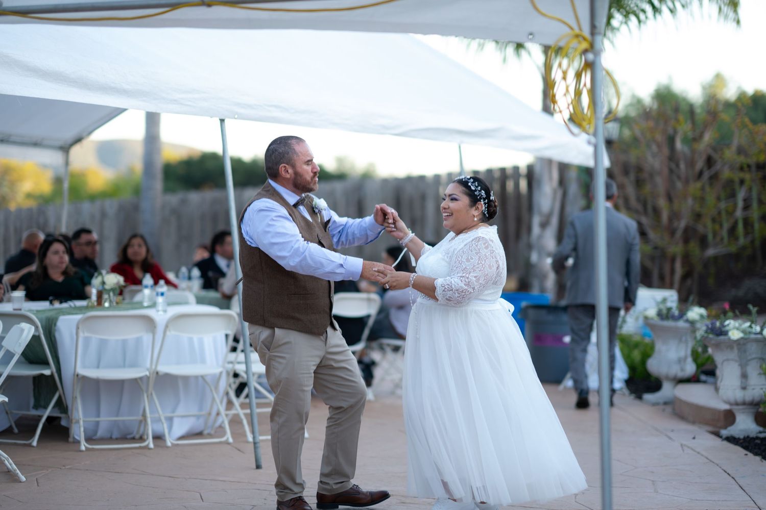 Wedding reception guests dance and celebrate under white outdoor tents during a festive evening celebration.