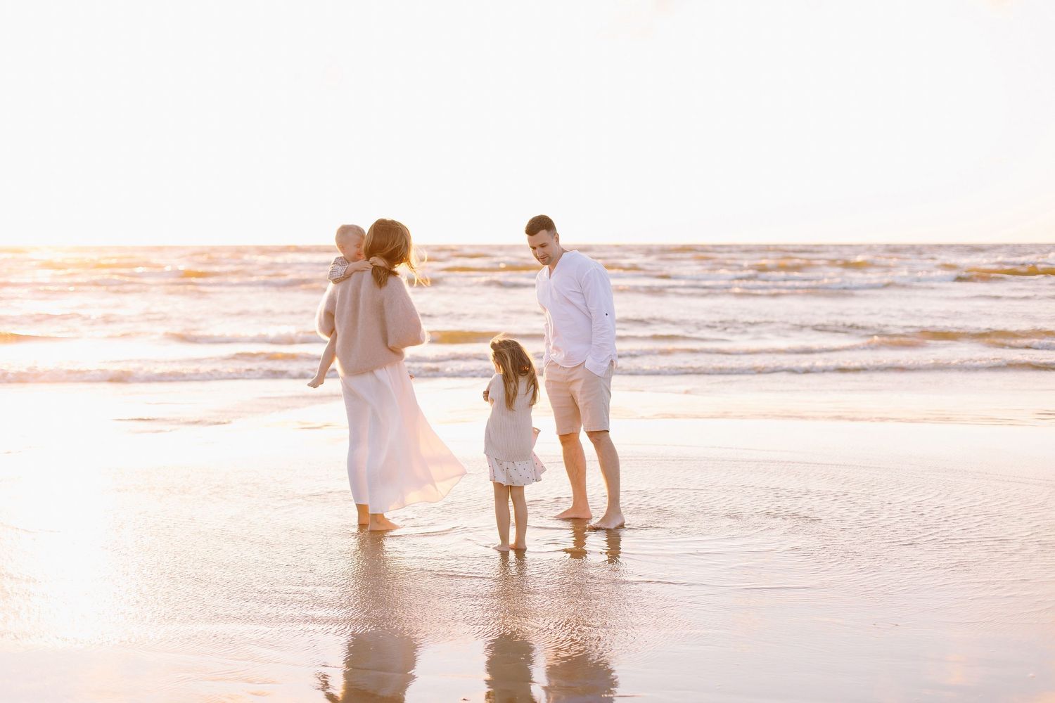 Family of four enjoying a sunset beach walk together, with waves gently lapping the shore in warm golden light.