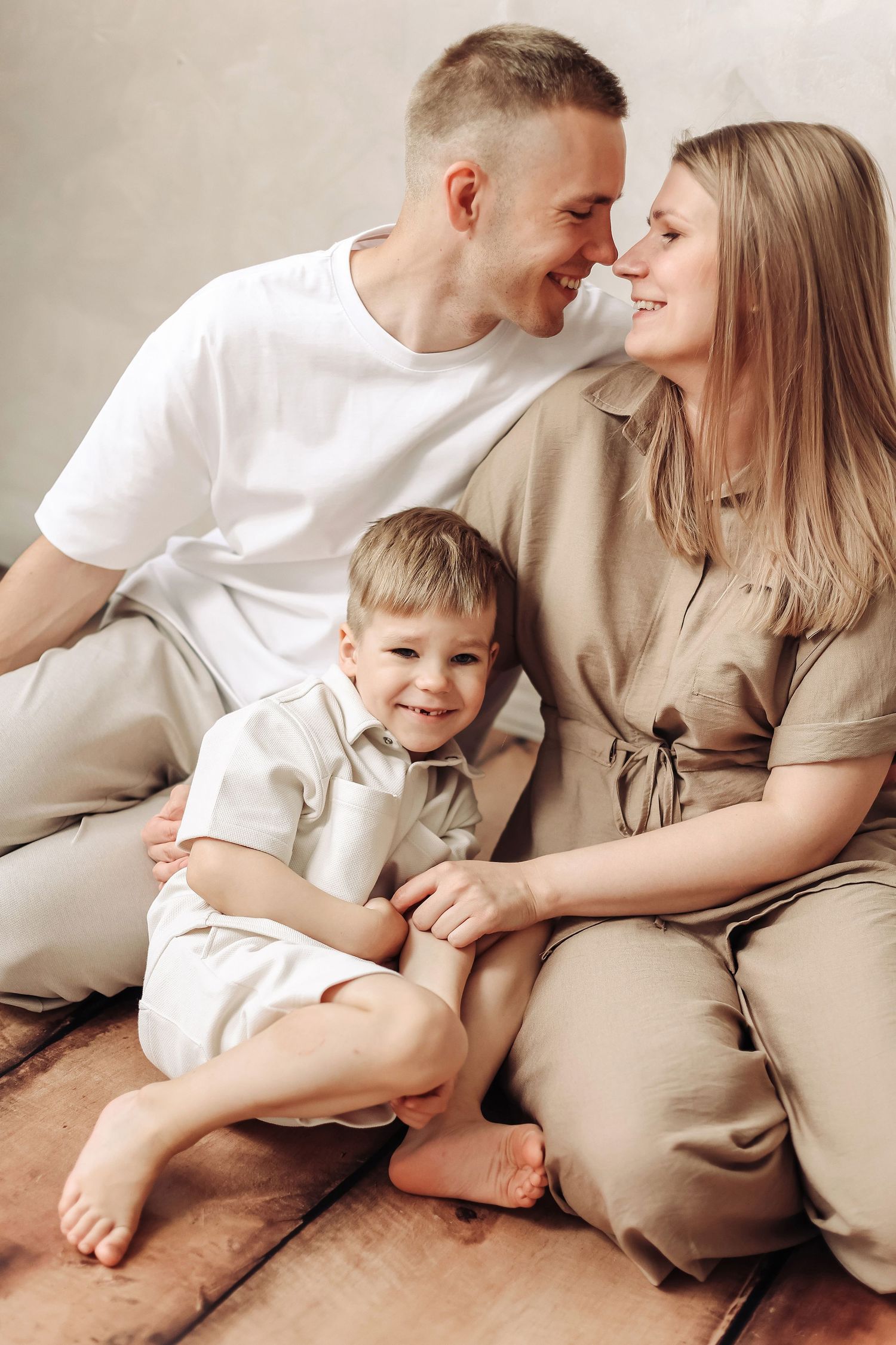 Happy family of three sitting together, parents sharing a tender moment while their smiling young son sits between them.