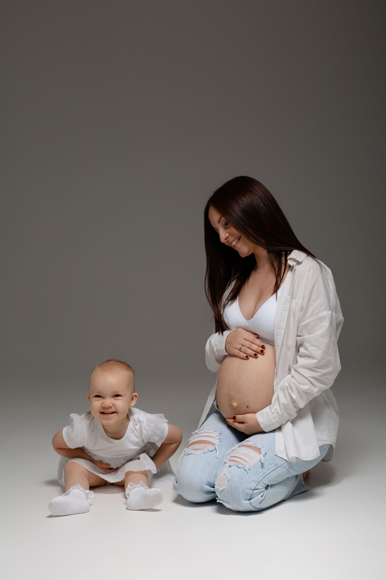 Grūtnieču fotosesija Rīgā studijā, sieviete elegantos, gaišos un tumšos toņos gaidībās.