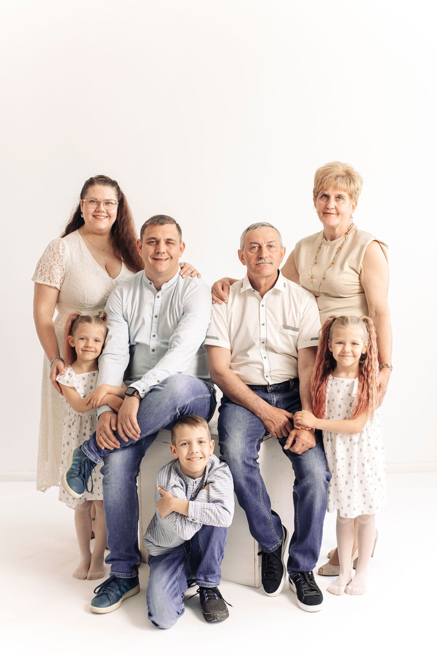Multi-generational family portrait with grandparents, parents, and three young children posing together against a white background.