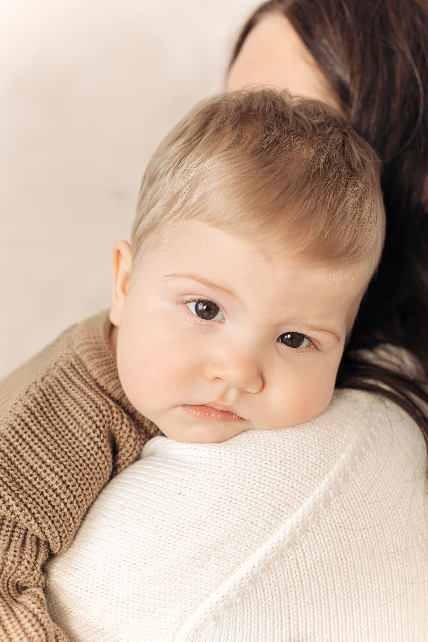 A tender moment of a baby resting on a mother's shoulder, with soft lighting and neutral tones.