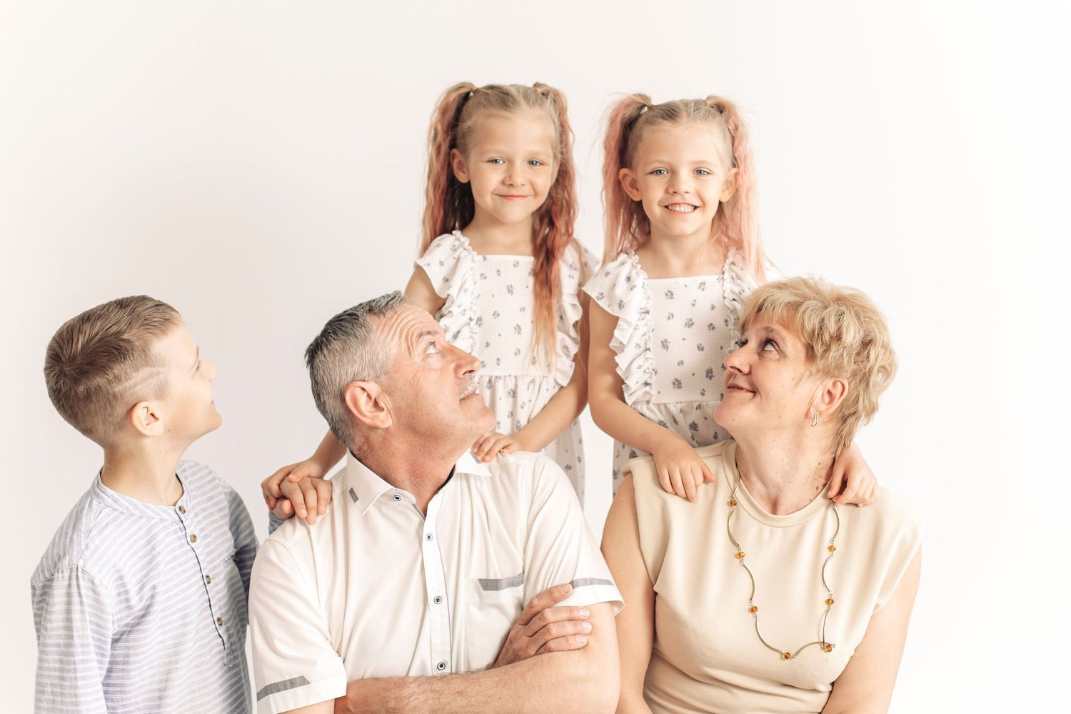 Grandparents smiling with three young grandchildren, two girls with pink pigtails and a boy, on white background.