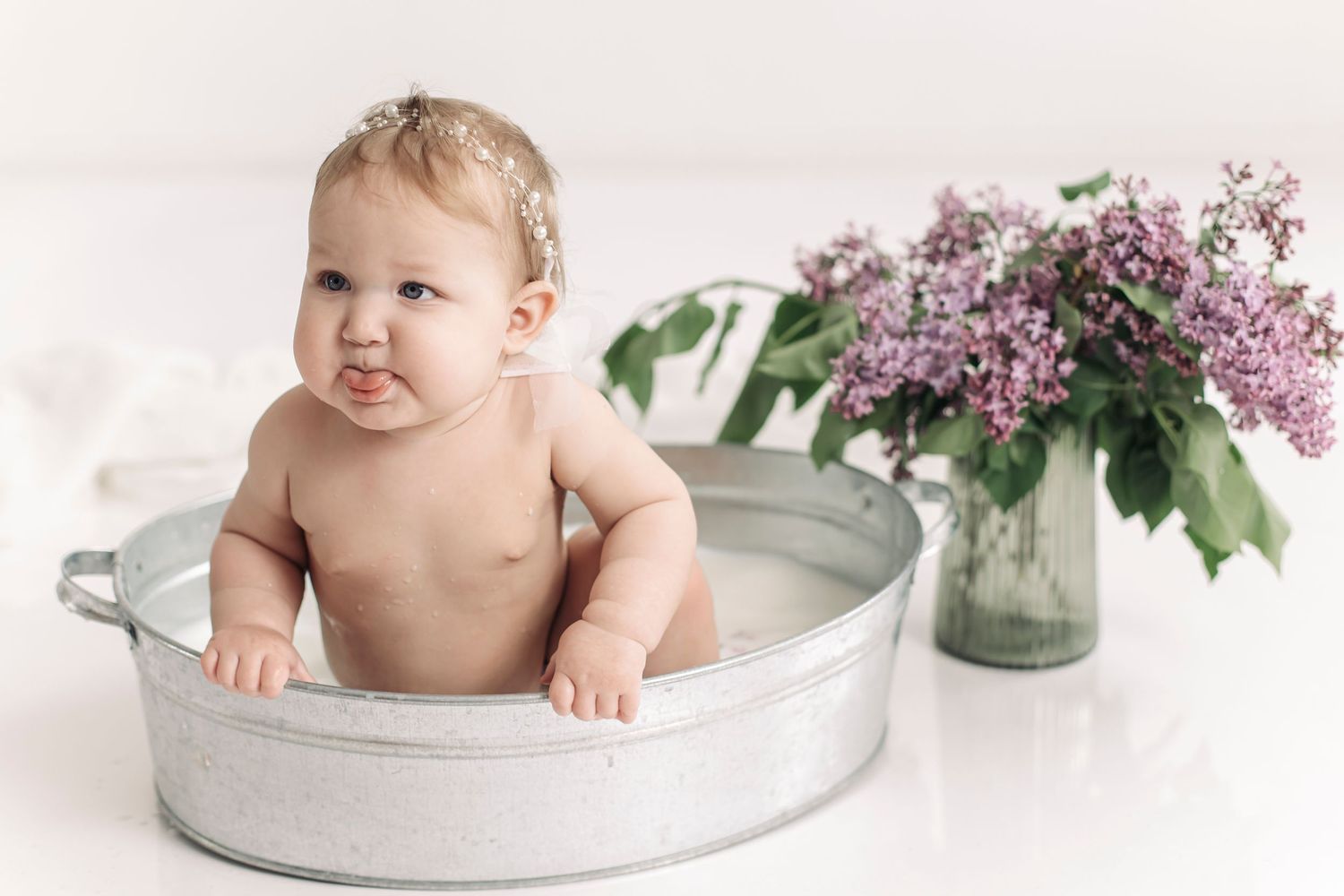 Cute baby sitting in a vintage metal tub with lilac flowers in background on white.