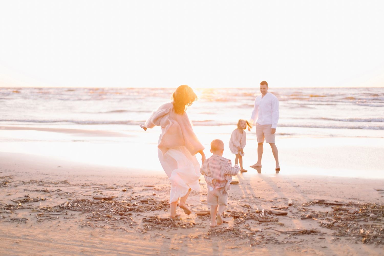 Family playing on a sunny beach at golden hour, with parents and children enjoying a joyful seaside outing.