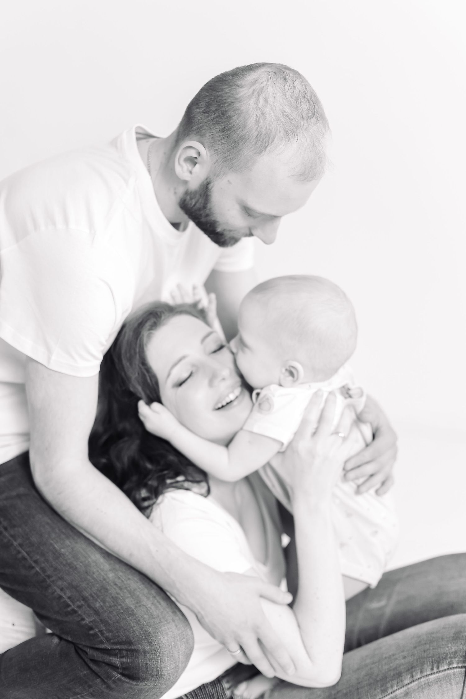 Black and white photo of a happy family with parents lovingly holding and kissing their newborn baby.