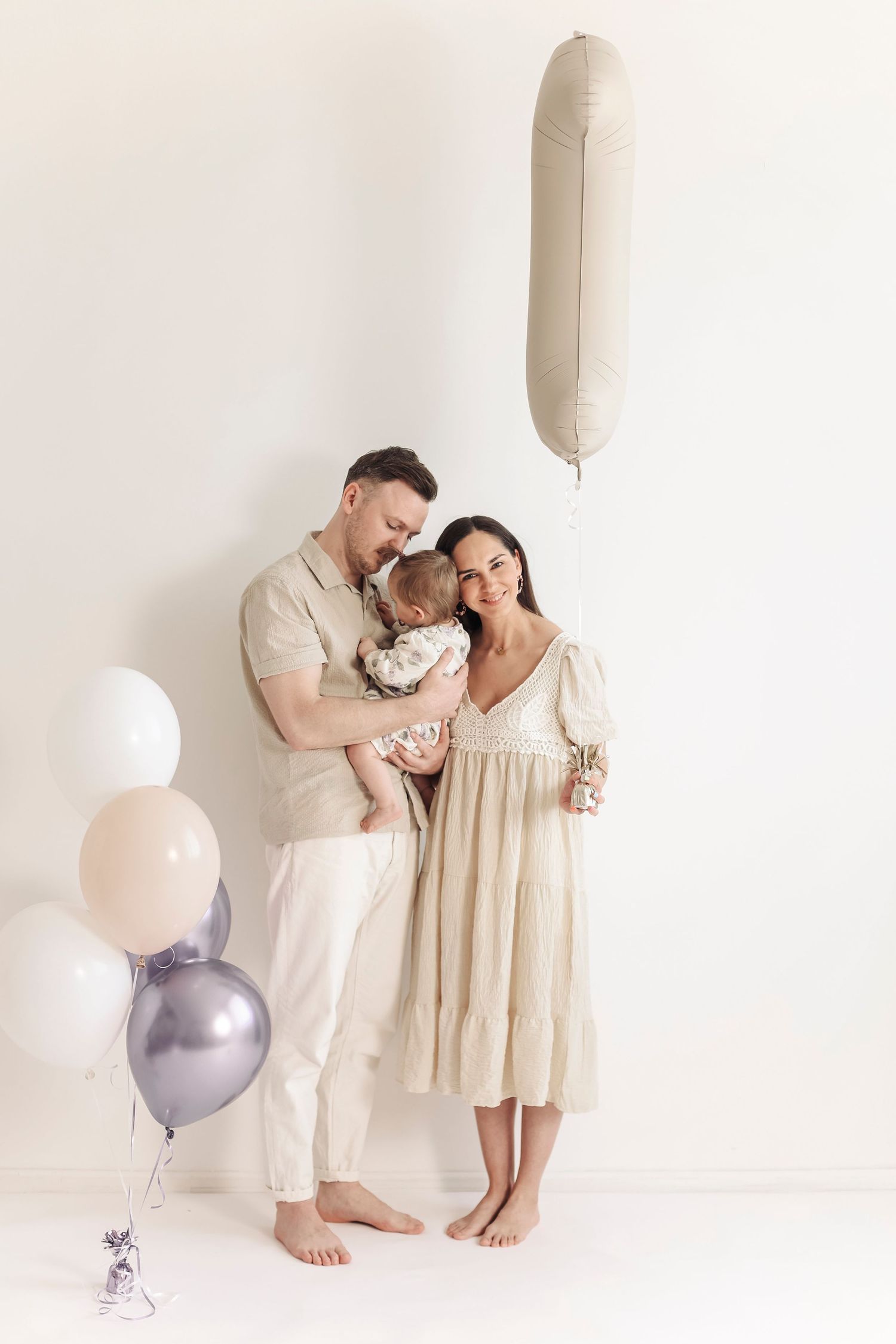Happy family with baby celebrating first birthday with beige balloons against white background.