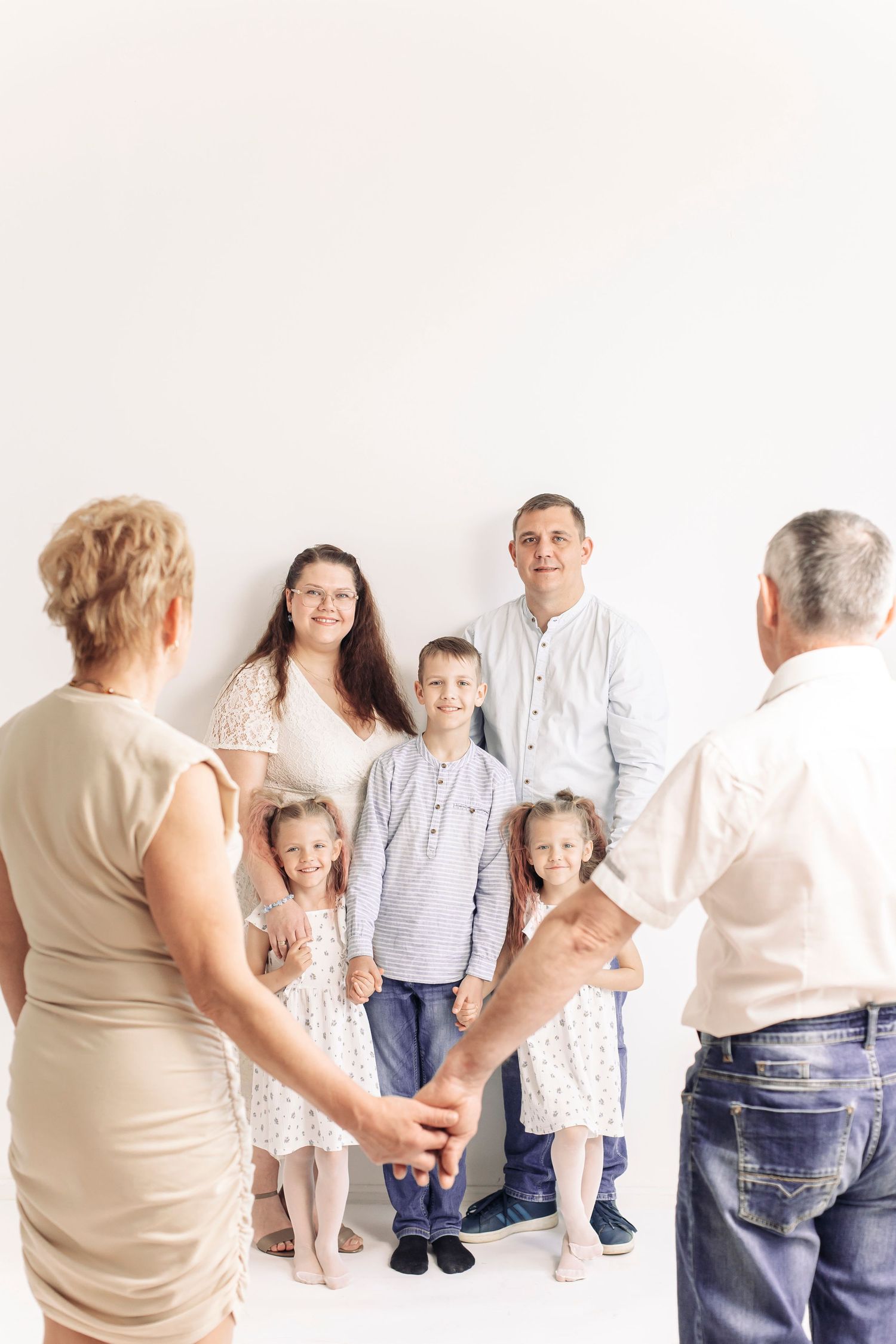 Multi-generational family portrait with grandparents, parents, and three young children posing together in a bright white studio.
