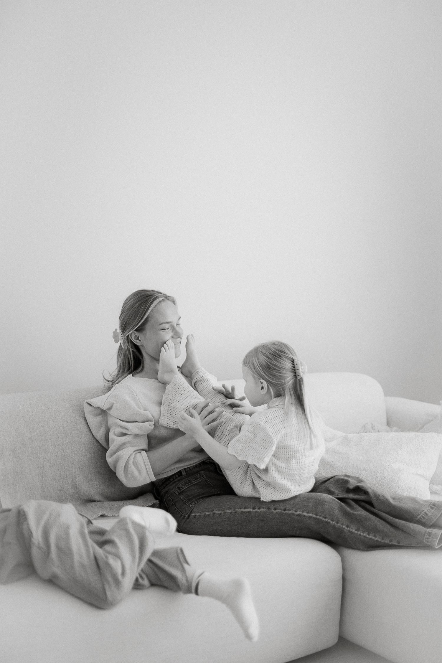 Black and white photo of a mother and daughter playing together on a cozy sofa at home.