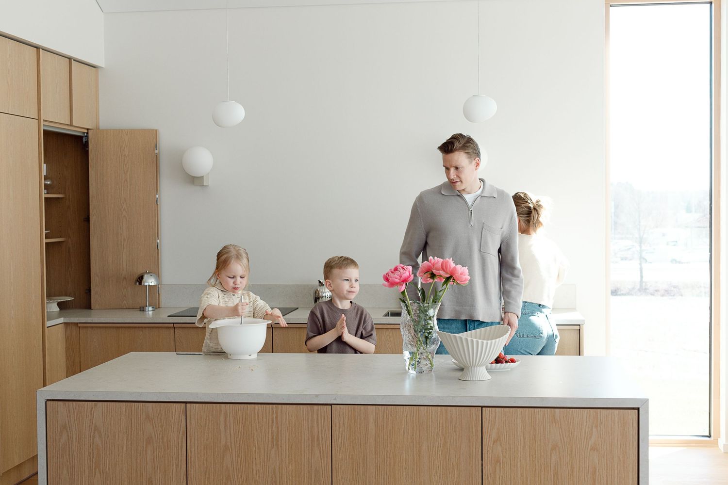 Family of four gathered around a modern kitchen island in a bright, minimalist white and wood kitchen.