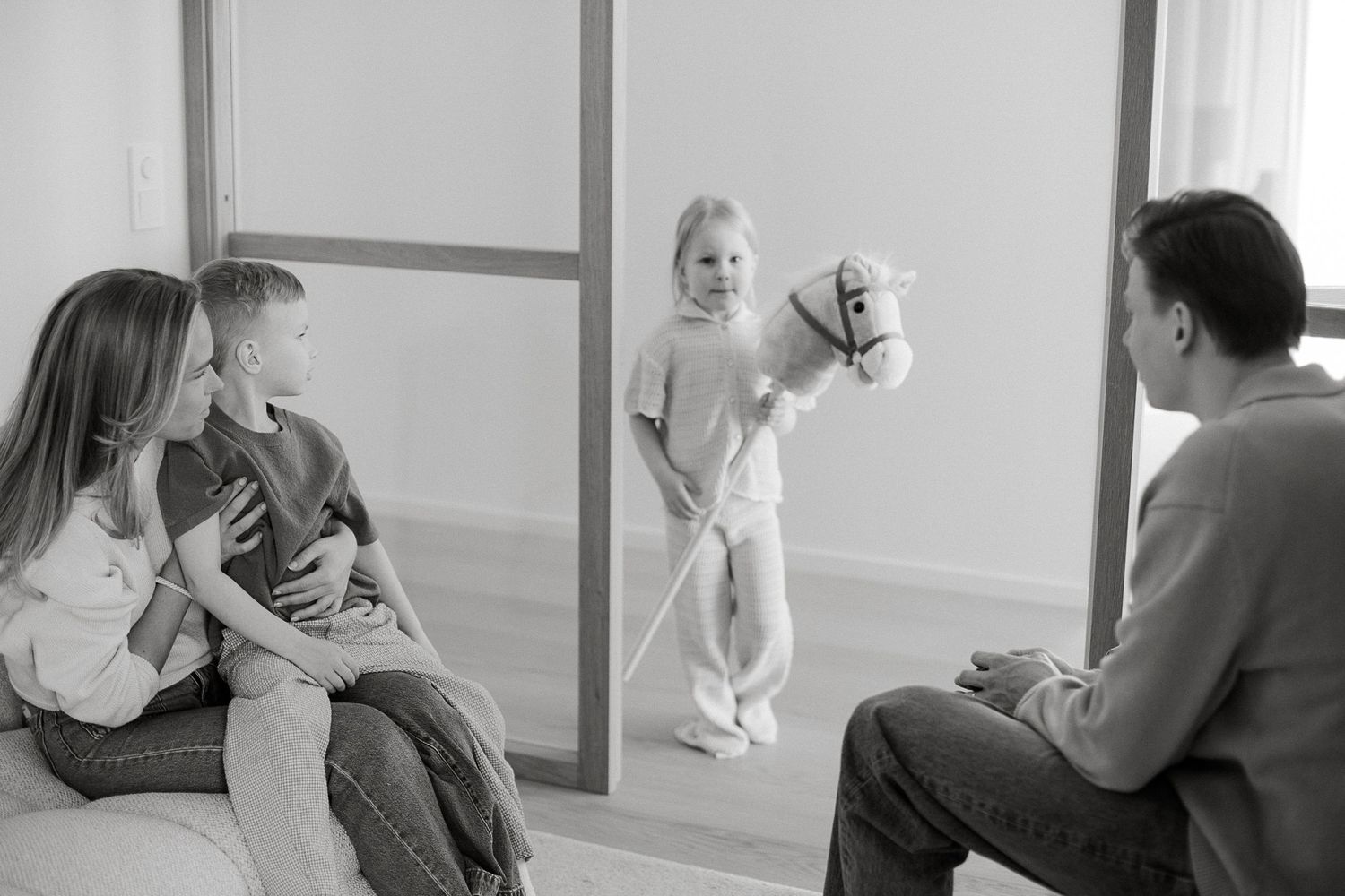 Family in therapy session with girl holding hobby horse toy while parents watch attentively in bright room.