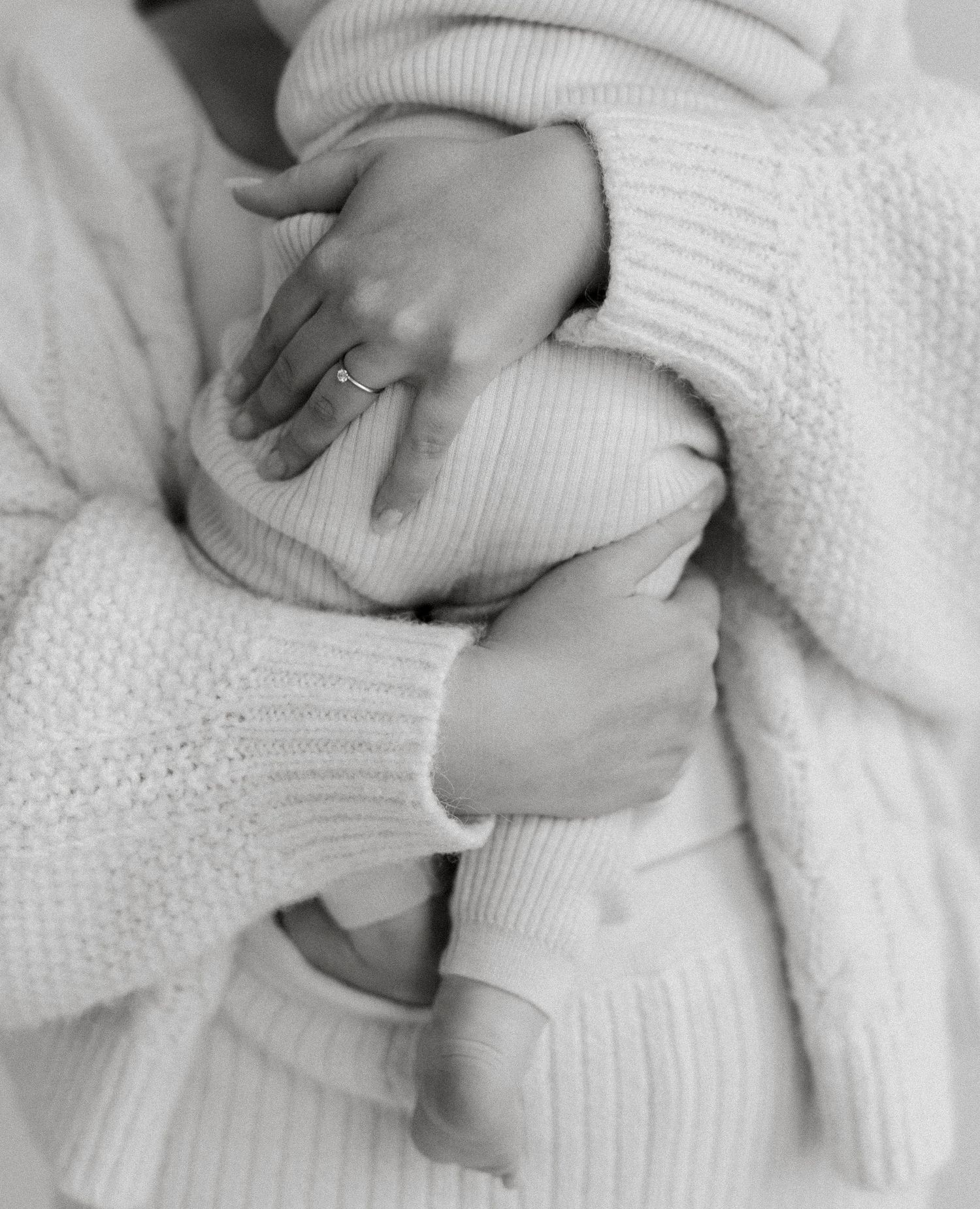 Black and white close-up of woman in knit sweater cradling baby with diamond ring visible.