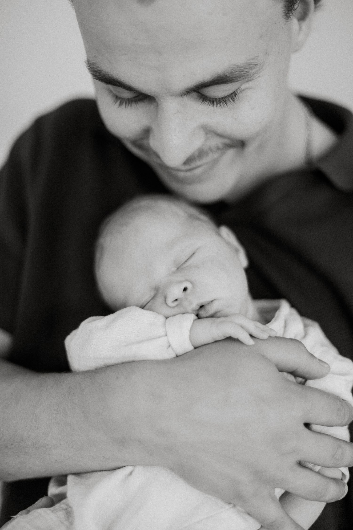 Black and white photo of a smiling parent cradling a sleeping newborn baby in their hands.