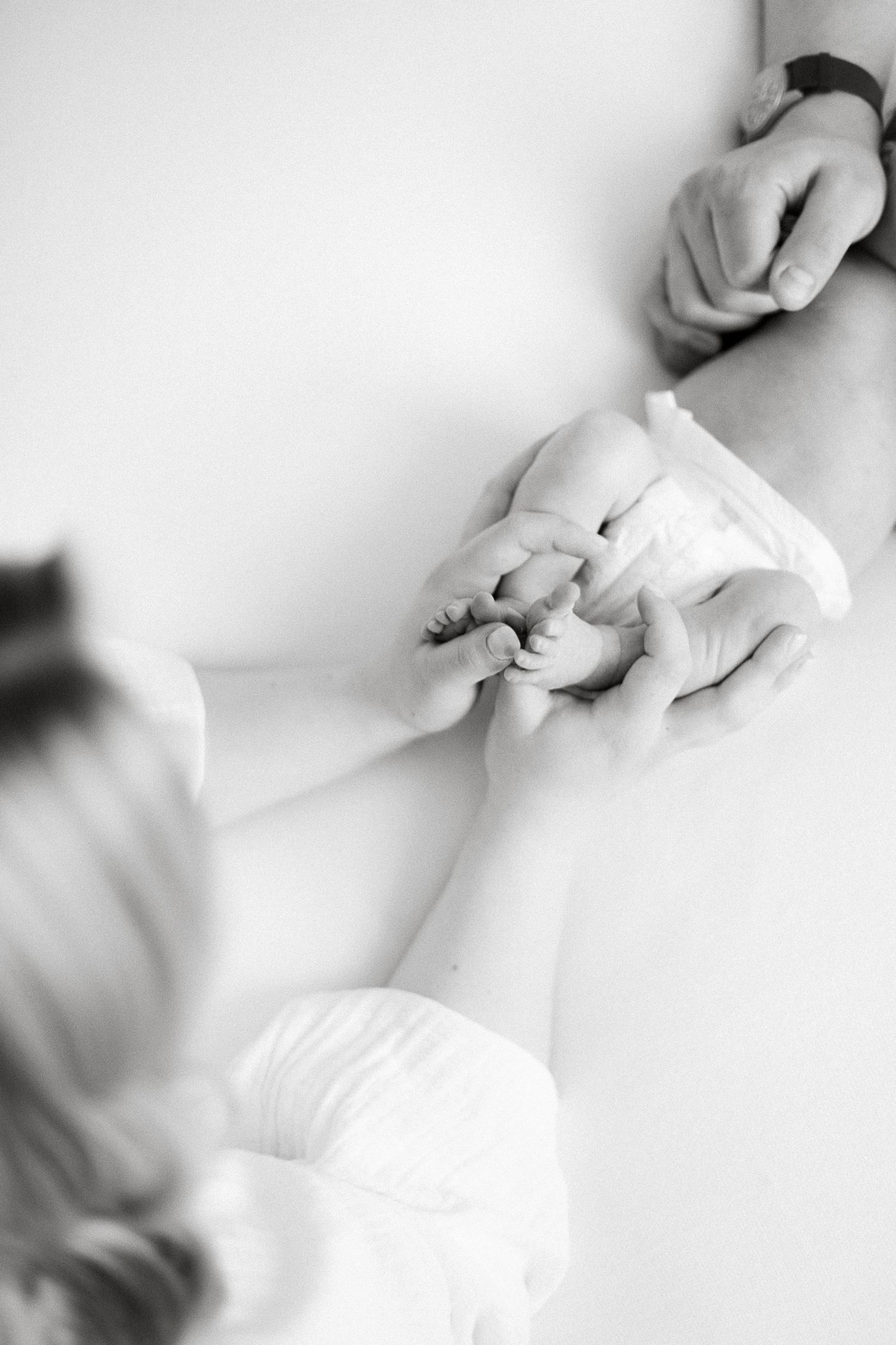 Black and white photo of parents tenderly holding their newborn baby's tiny feet together.