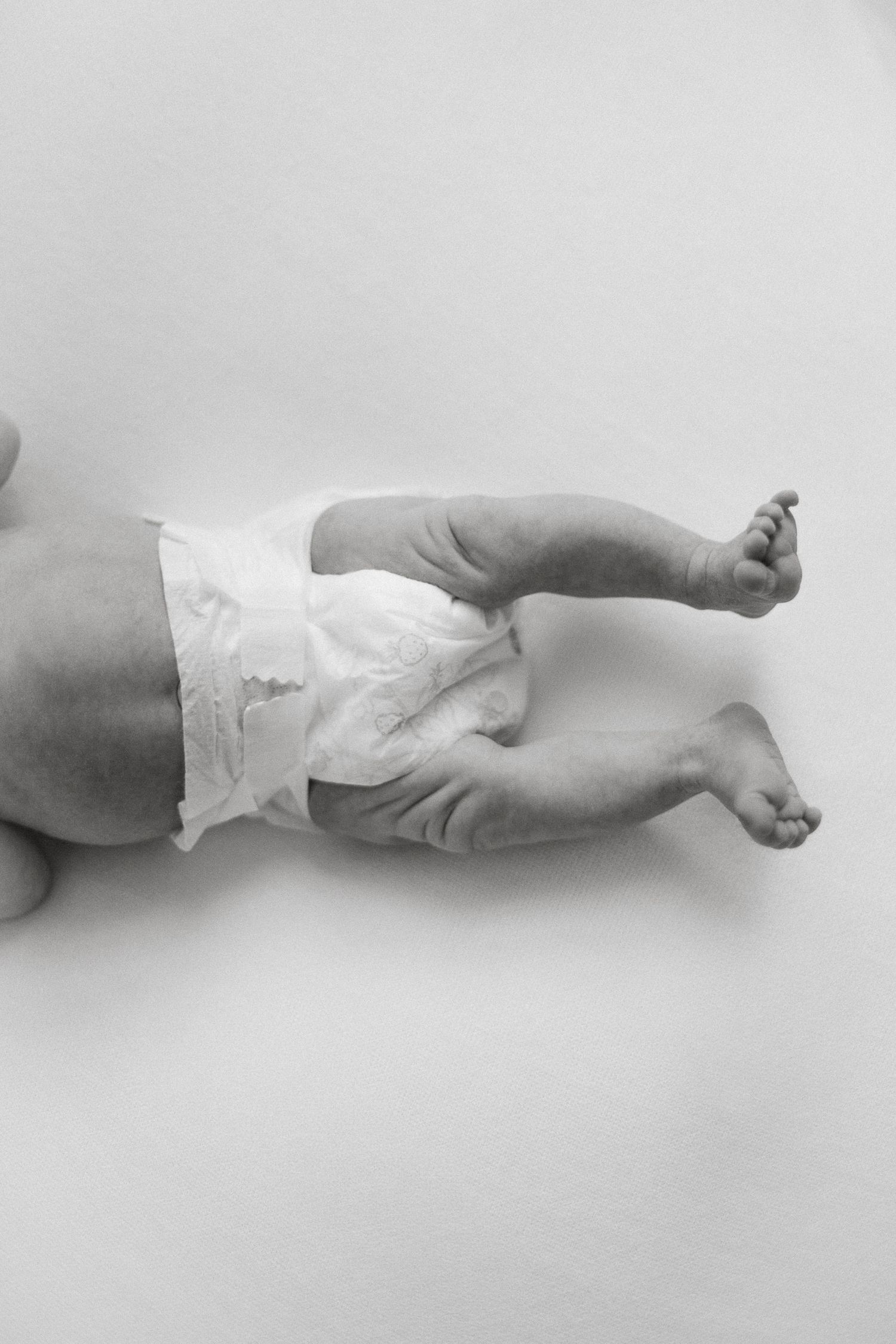 Black and white close-up photo of a newborn baby's legs and diaper on a white background.