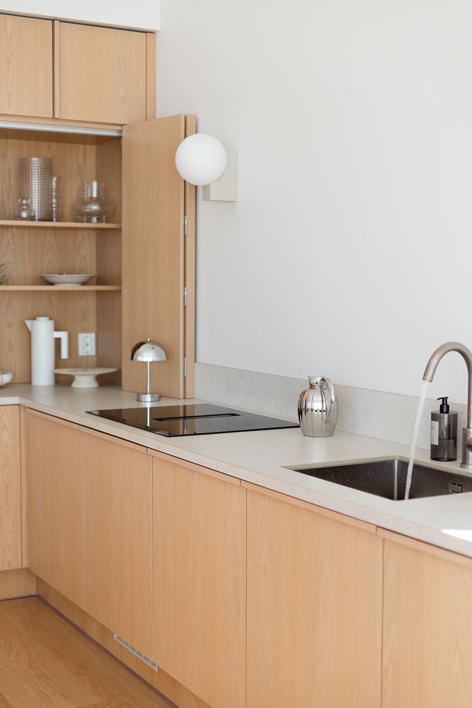 Modern Scandinavian kitchen with light oak cabinets, stone countertops, induction cooktop, and undermount sink with brass faucet.