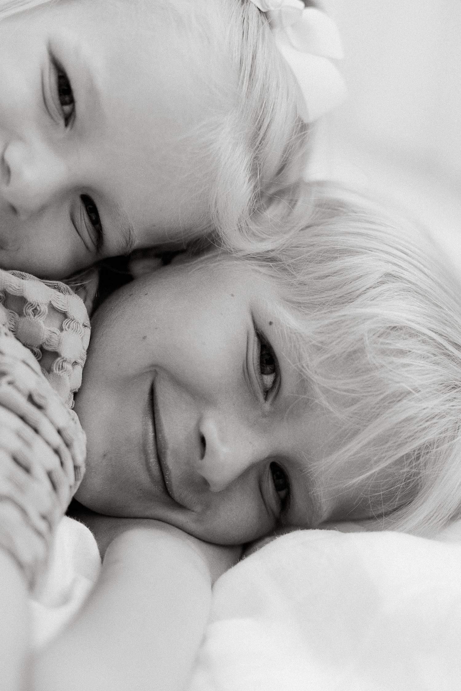 Two young blonde children cuddle together in a tender black and white portrait photograph.